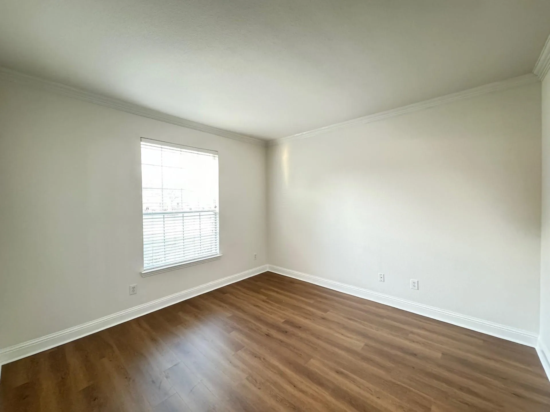 Wood-finish flooring, white walls, and a window with horizontal blinds