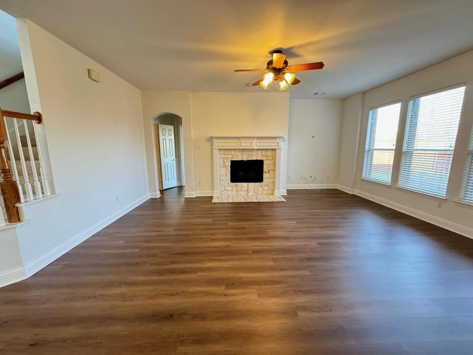 Spacious living area featuring wood-finish flooring, a fireplace with a stone surround, multiple windows, and a ceiling fan