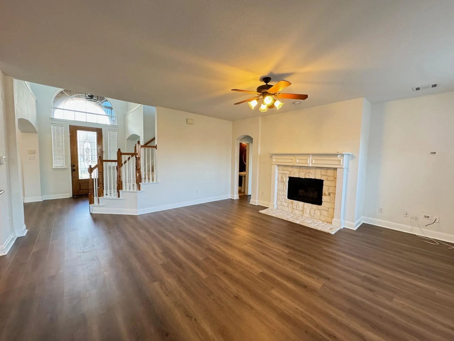 Wood-finish flooring throughout, featuring a fireplace with a stone surround and mantle, and a ceiling fan with integrated lighting