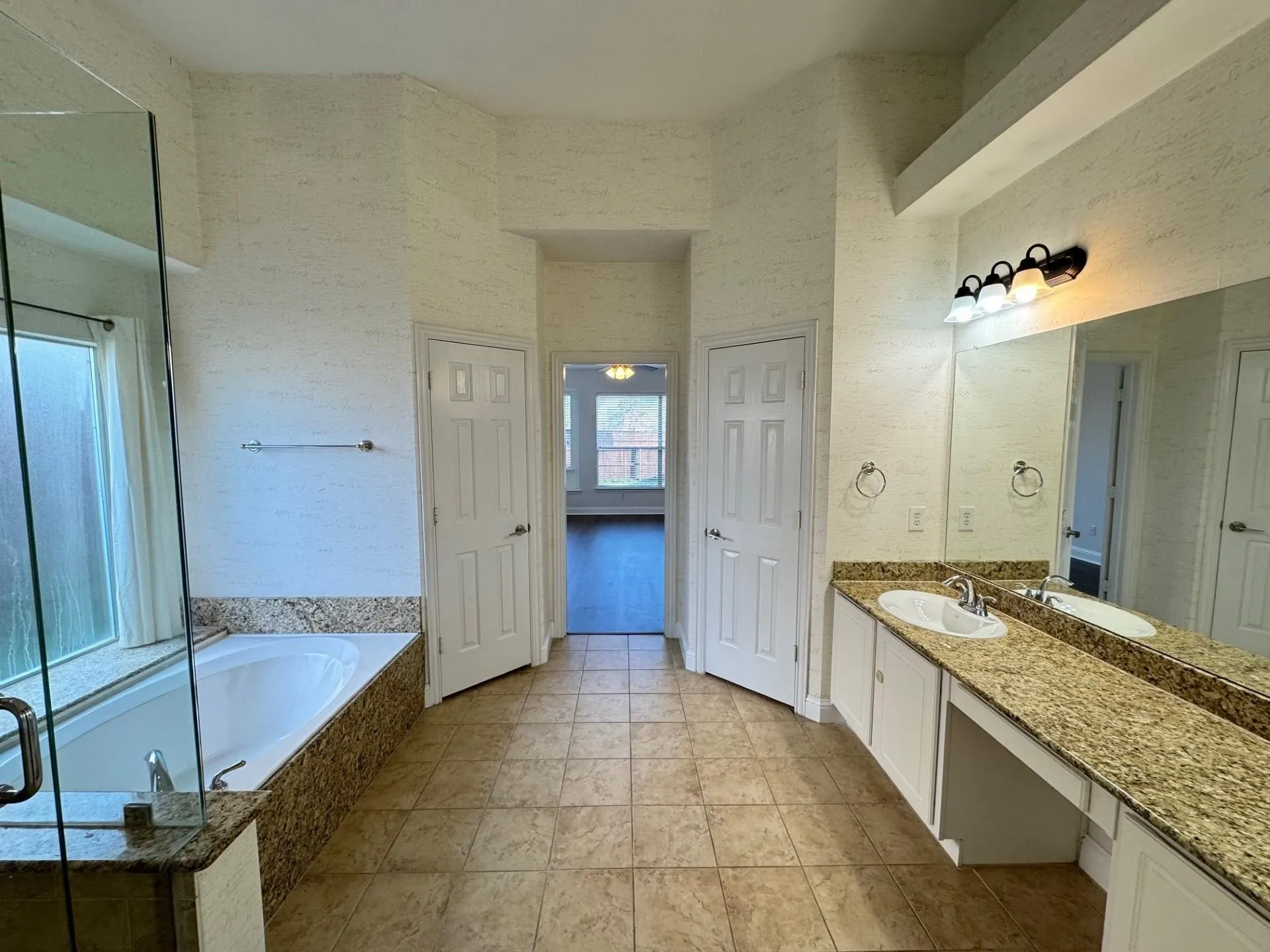 Expansive bathroom featuring a built-in soaking tub, glass-enclosed shower, dual vanity with undermount sinks, and a large wall mirror
