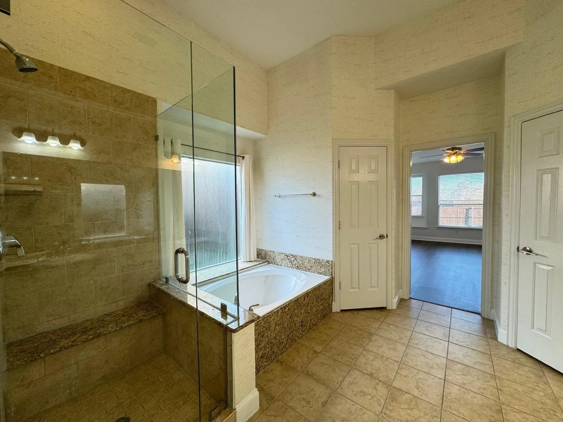 Tiled flooring and a built-in soaking tub complement the glass-enclosed shower, featuring a built-in bench and tiled walls