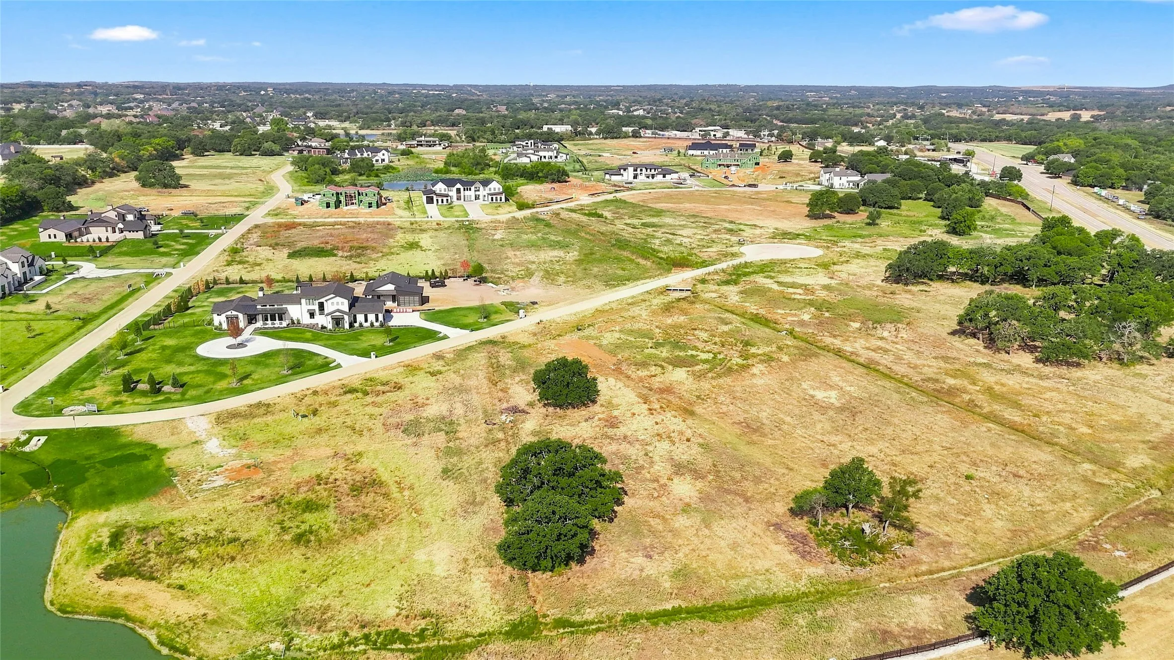 Expansive land parcel featuring existing residential structures, scattered mature trees, and a visible roadway