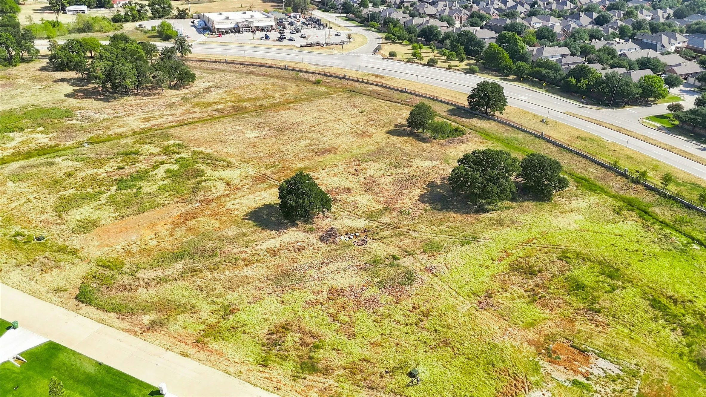 Expansive undeveloped land featuring natural vegetation and scattered mature trees, bordered by roadways and a residential community