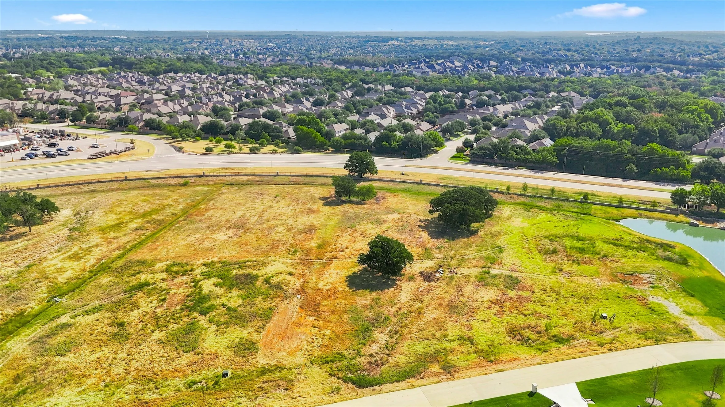 Expansive undeveloped parcel with a natural pond and established trees, bordered by a paved road and residential developments