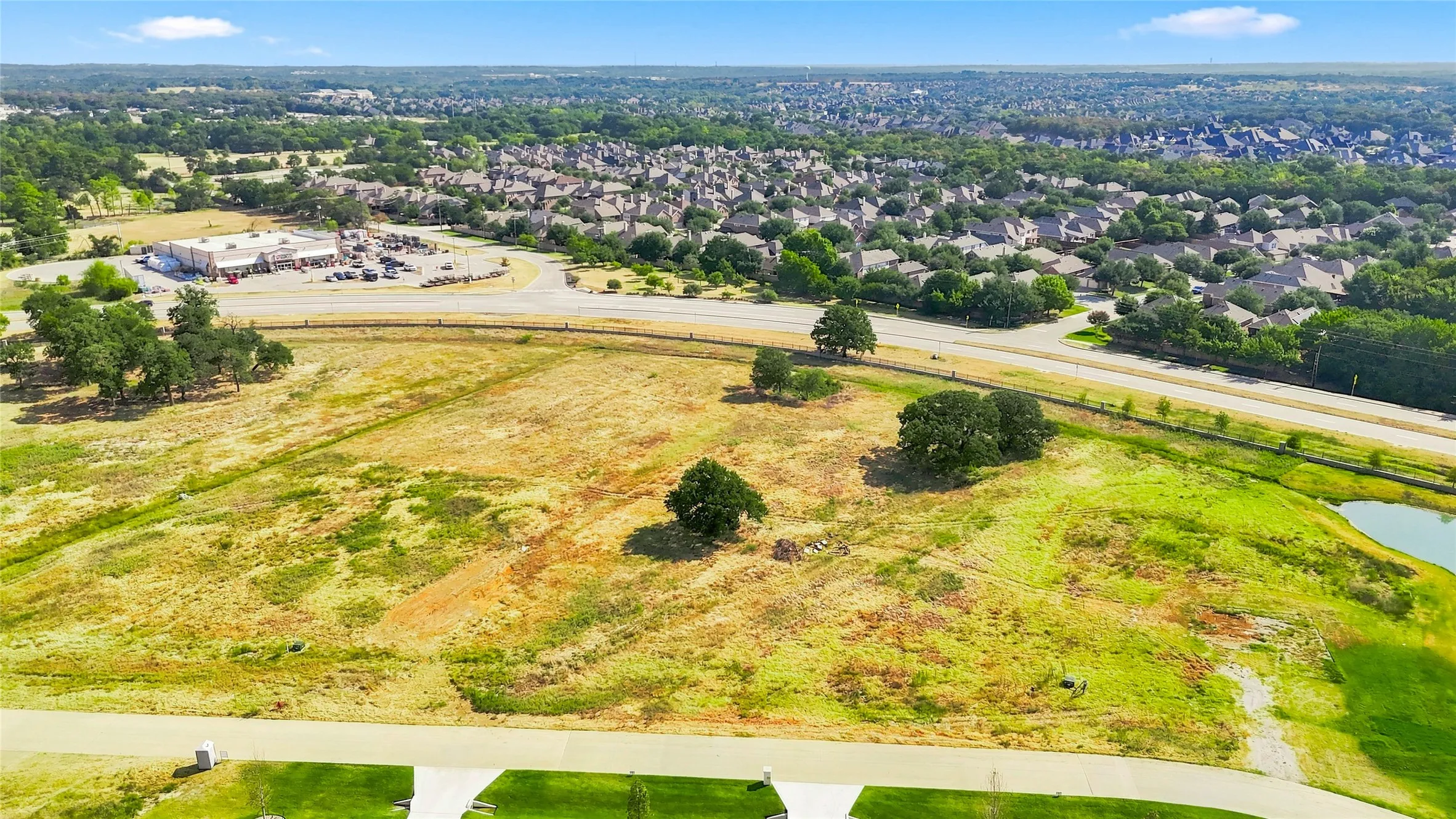 Expansive undeveloped land featuring natural vegetation, scattered mature trees, and a visible roadway