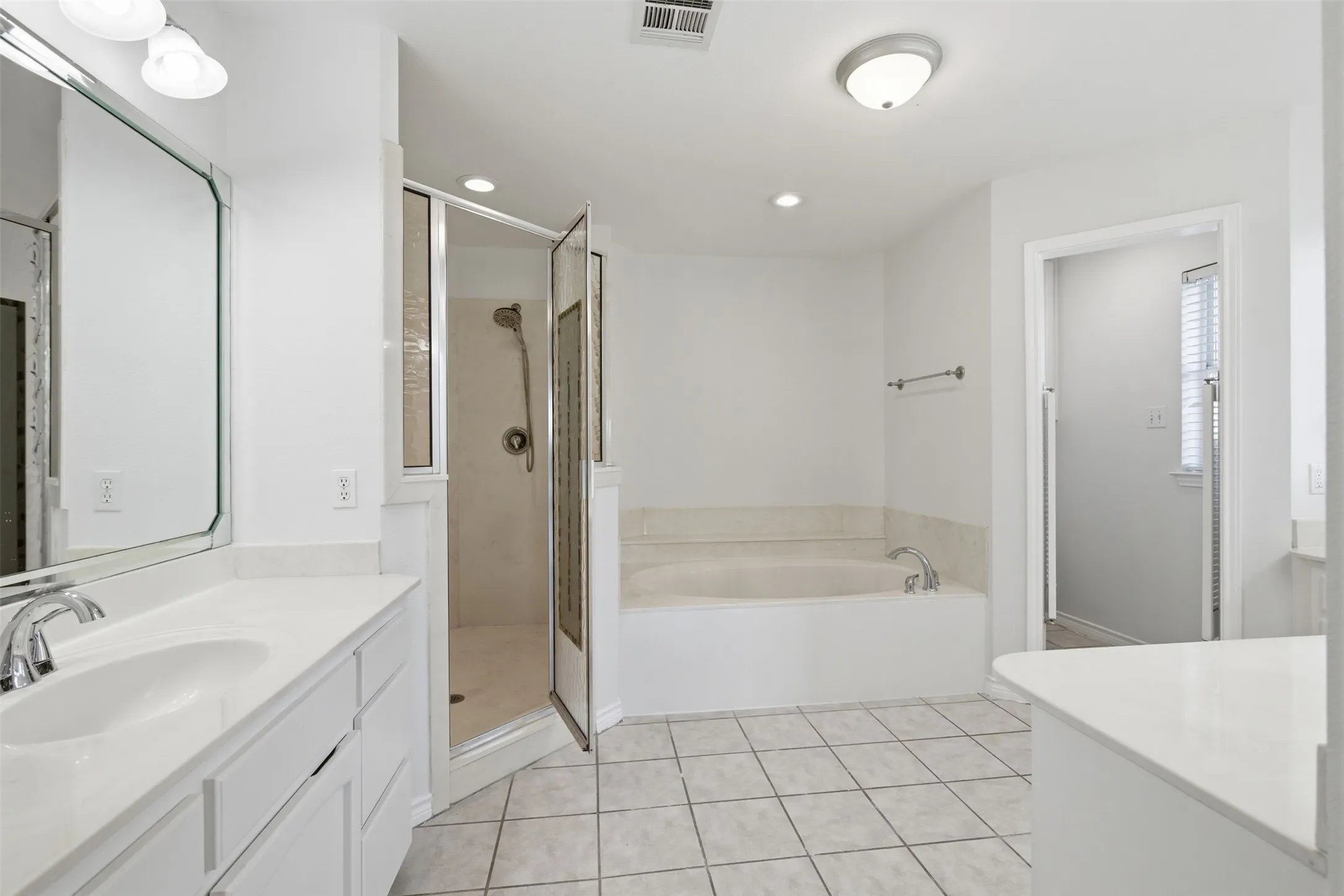 Double vanity with chrome fixtures and integrated sinks, a walk-in shower with clear glass enclosure, a built-in bathtub, and ceramic tile flooring