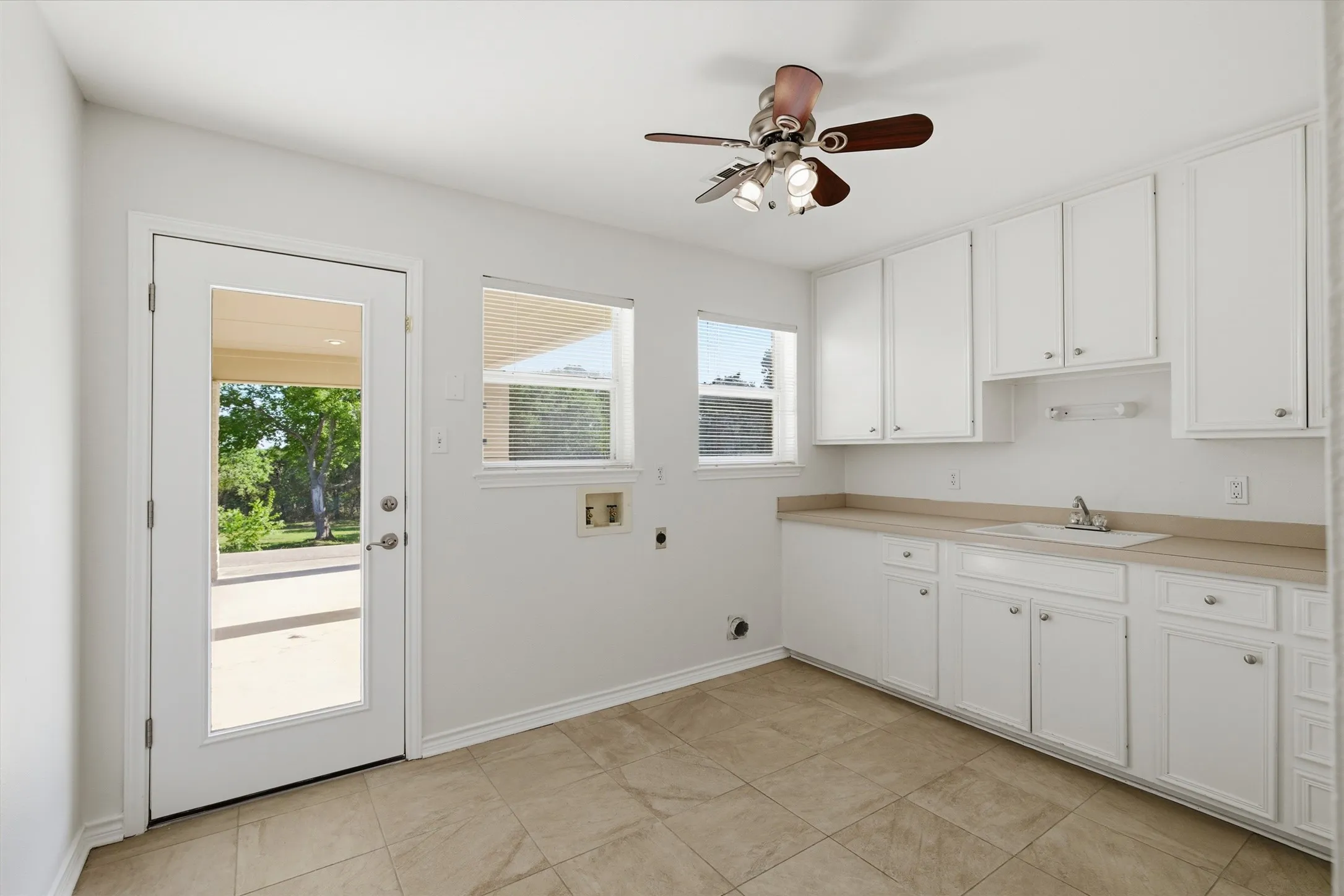 Tile flooring, a full-lite exterior door, dual windows, and white cabinetry with an integrated sink