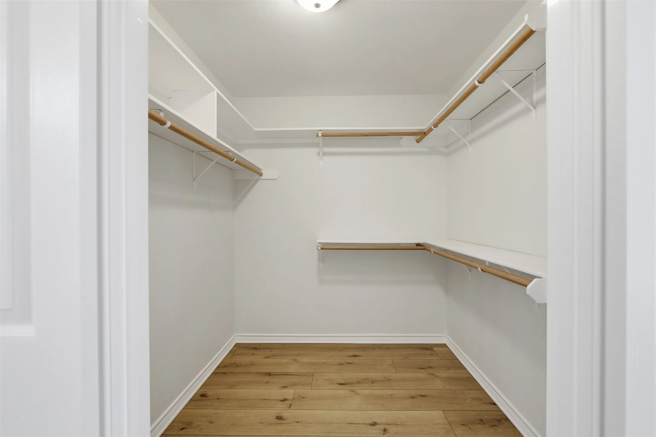 Walk-in closet featuring white shelving, wood-finish flooring, and a flush-mount ceiling light