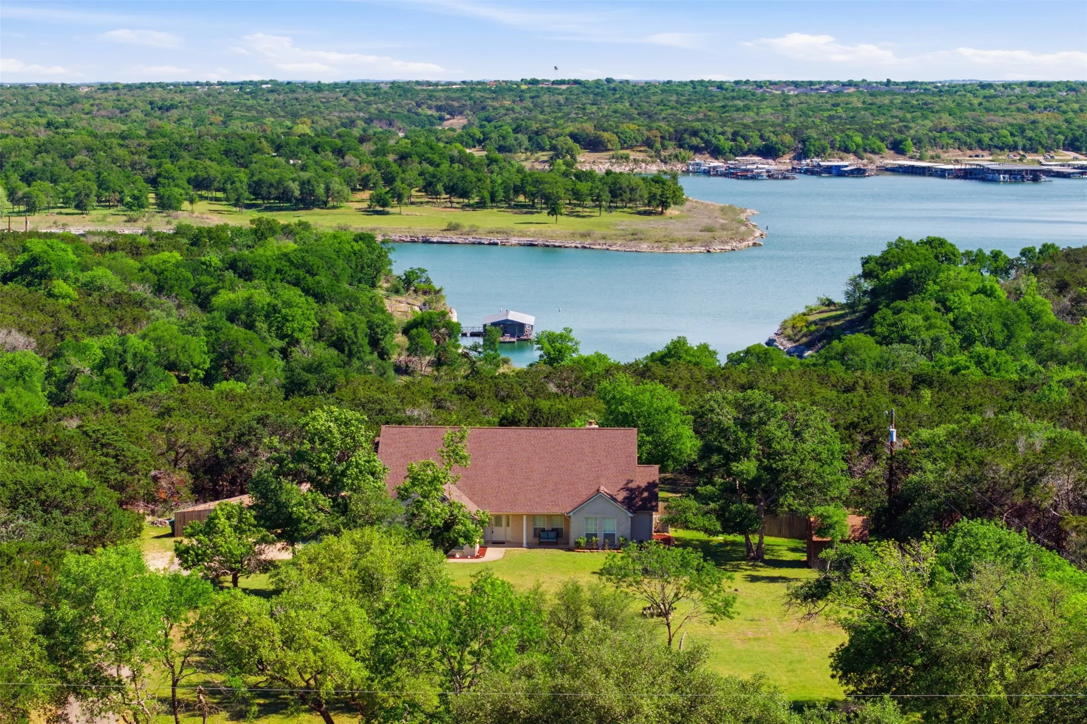 Waterfront property with a brown shingle roof, surrounded by mature trees and a manicured lawn