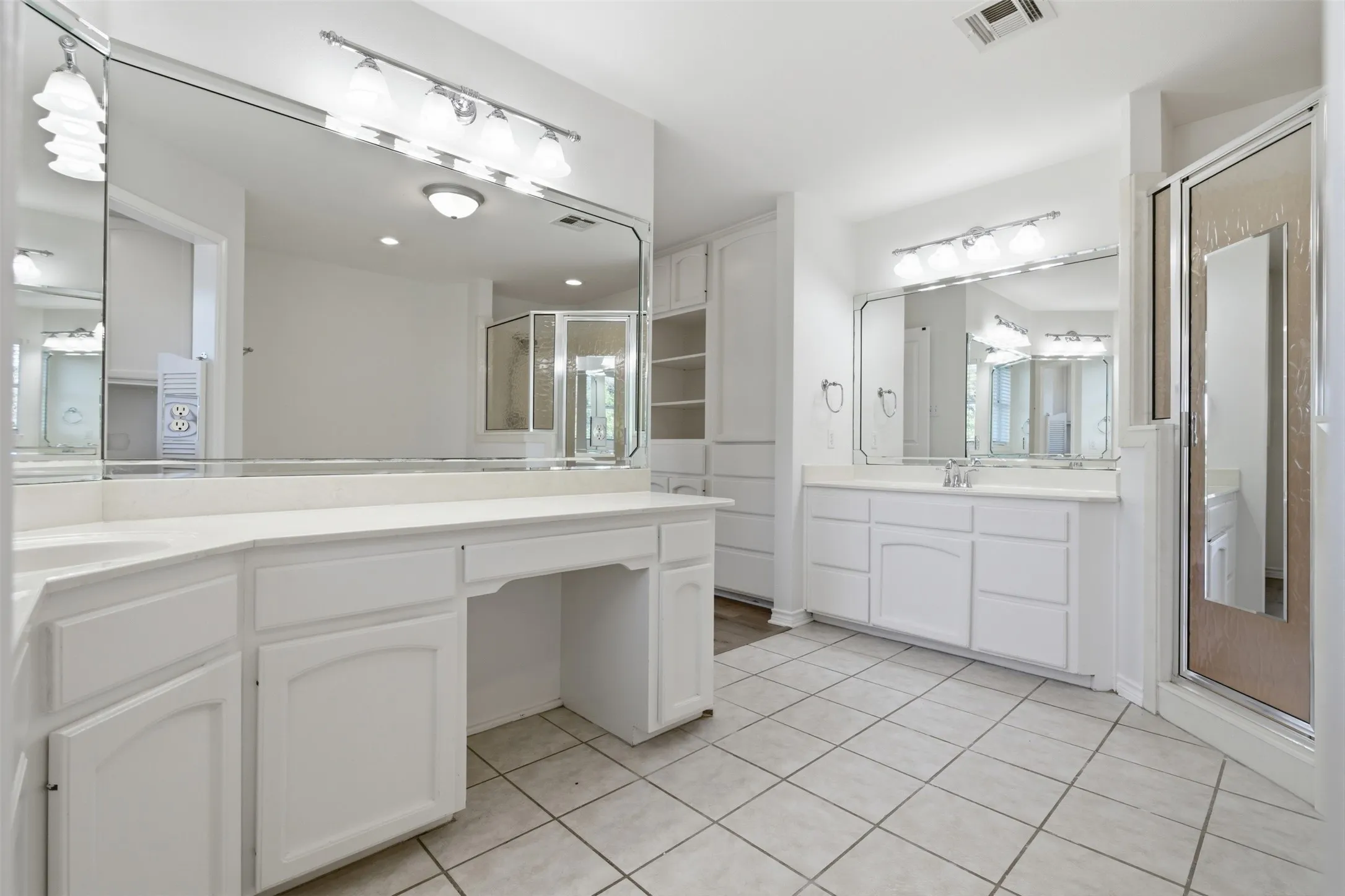 Expansive bathroom featuring dual vanities with integrated sinks, a built-in makeup vanity, a glass-enclosed shower, and built-in shelving