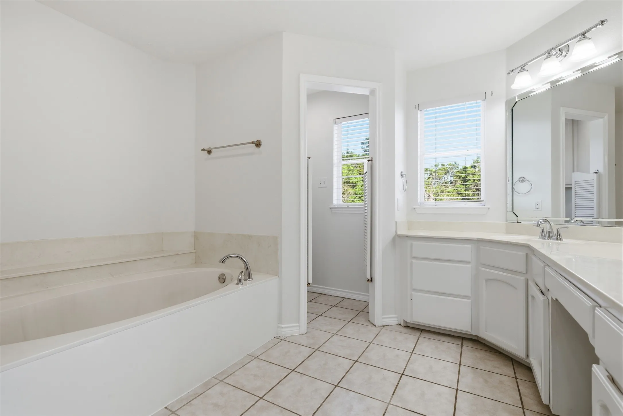 Built-in bathtub with polished chrome fixtures, dual vanity with white cabinetry, integrated countertop, and tiled flooring
