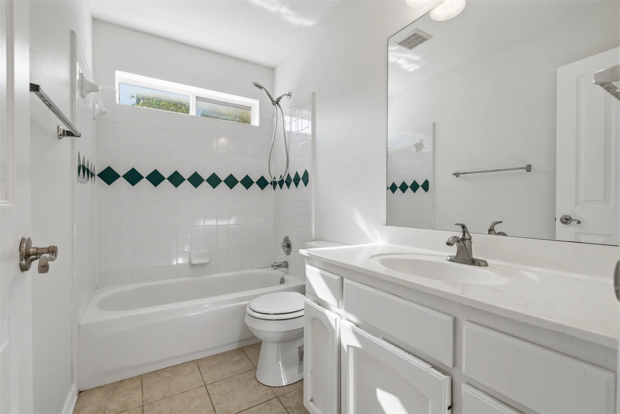 Full bathroom featuring a white vanity with integrated sink, a bathtub with shower, ceramic tile flooring, and white wall tiling with a decorative accent band