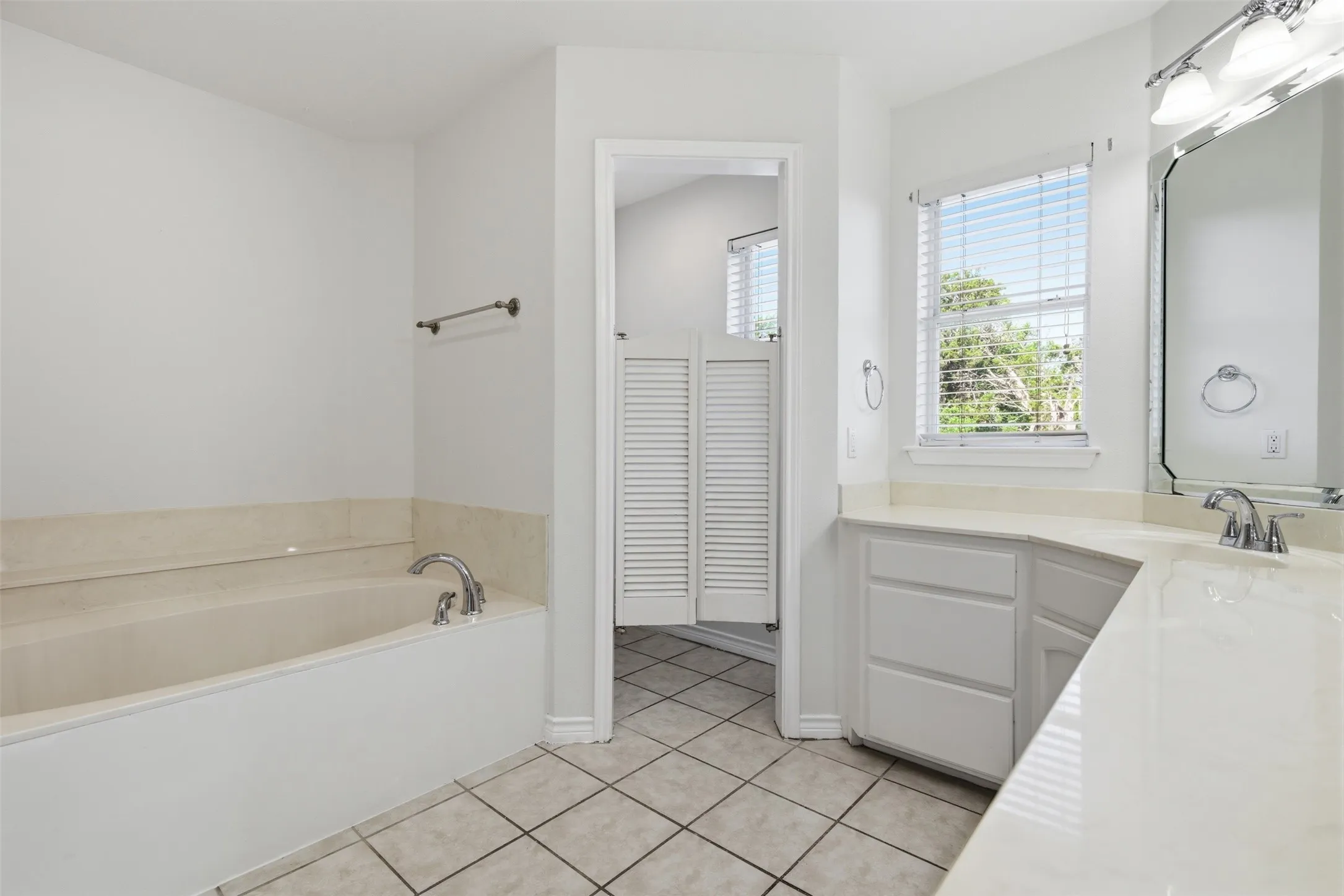 Built-in soaking tub, dual vanity with integrated sinks, framed mirror, tiled flooring, and privacy shutters