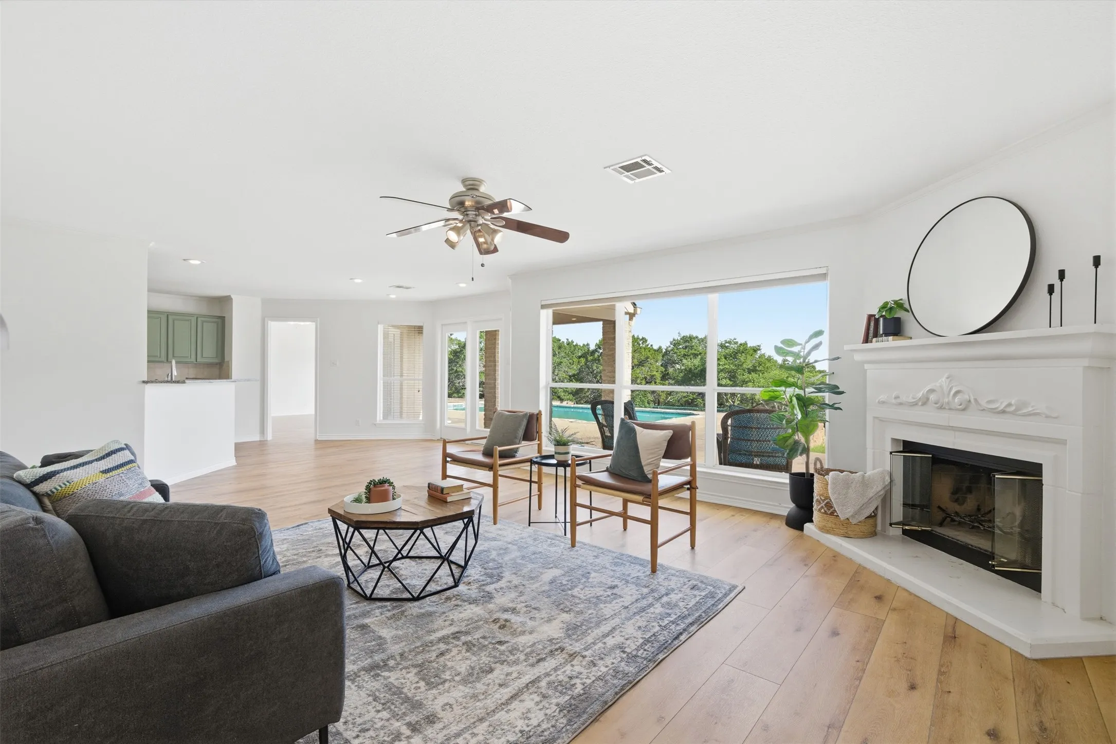 Spacious living area featuring wood-finish flooring, a fireplace with a decorative mantel, and abundant natural light from large windows