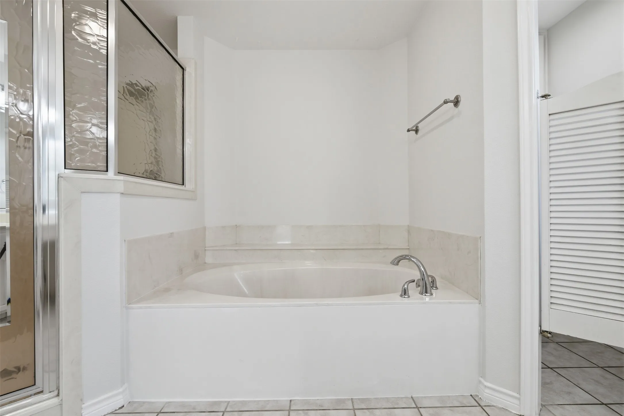 Soaking tub with deck-mounted chrome fixtures, surrounded by a tiled enclosure