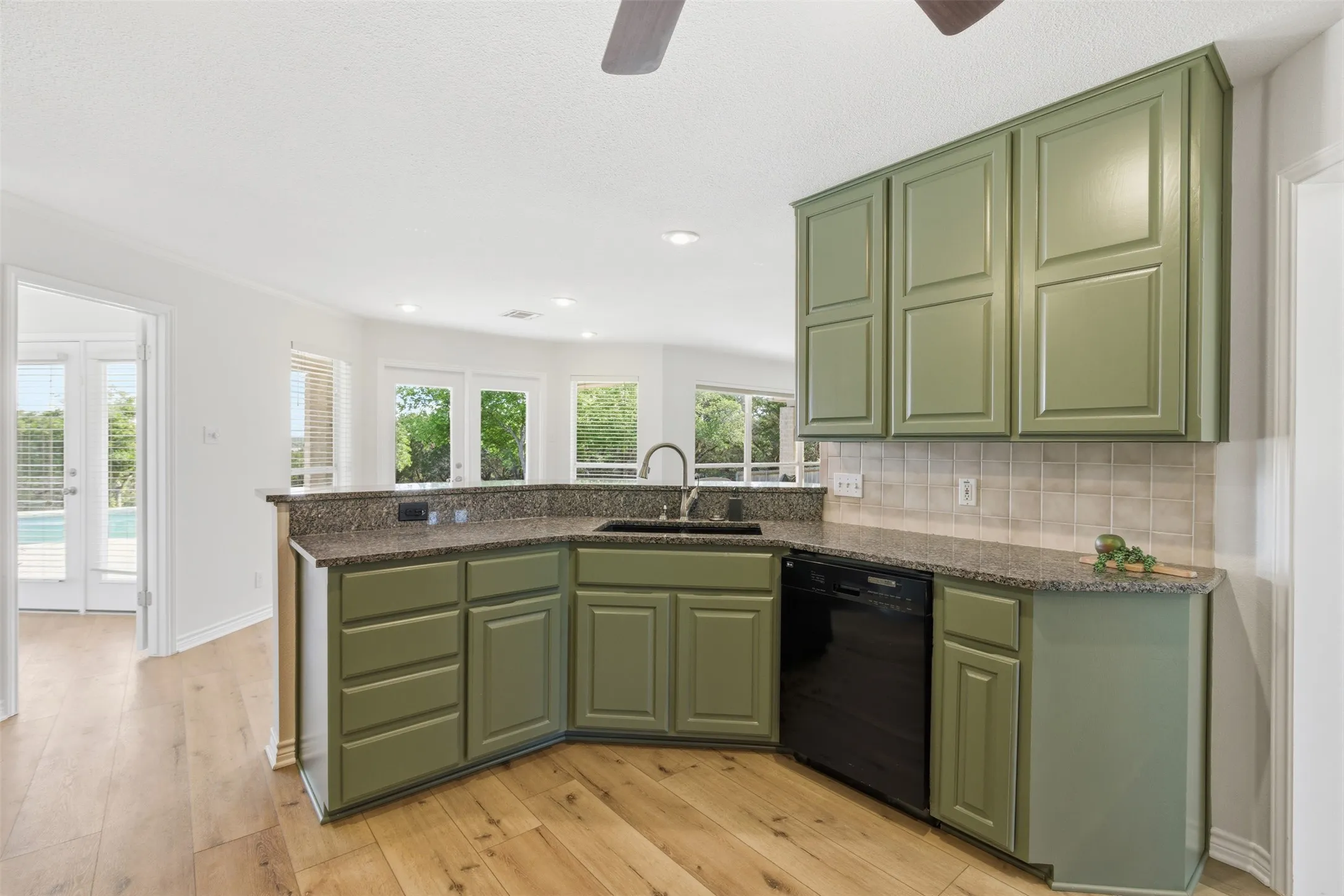 Kitchen featuring green cabinetry, dark granite countertops, neutral tile backsplash, and a built-in black dishwasher