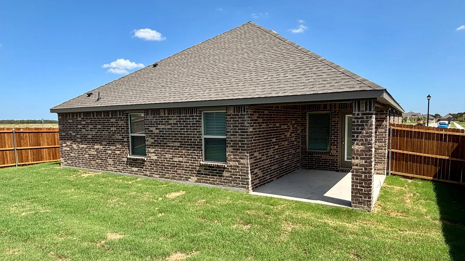 Brick exterior with a covered patio, shingle roof, and privacy fencing