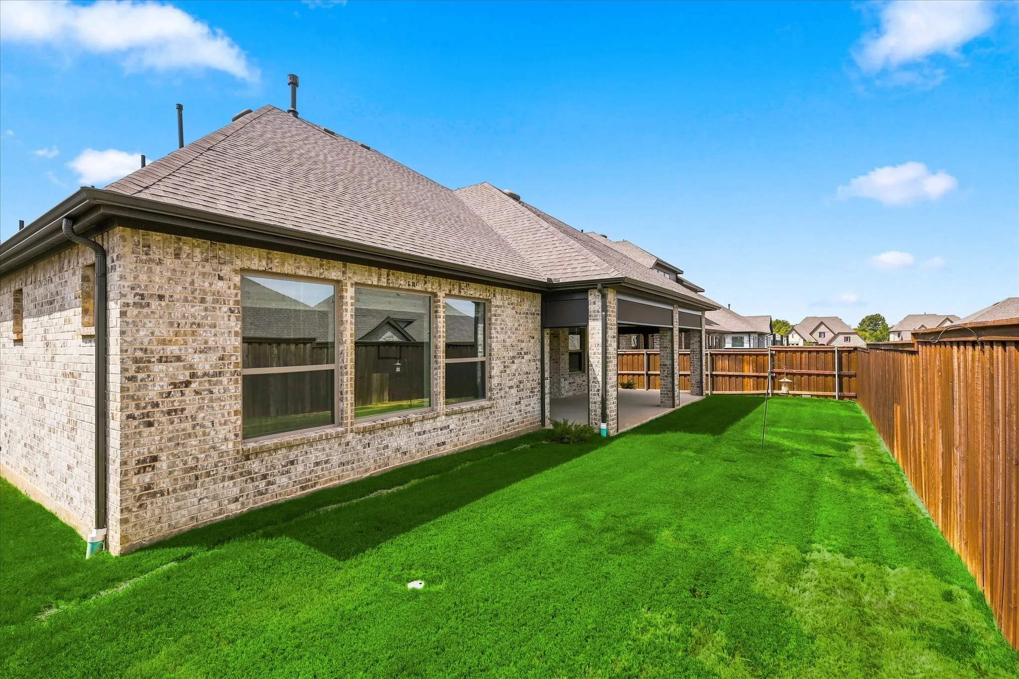 Expansive backyard featuring a manicured lawn, full privacy fencing, and a covered patio area