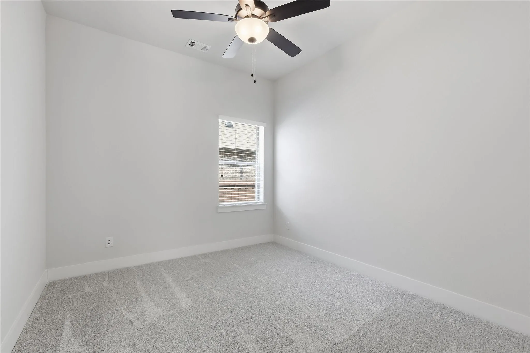 Neutral wall paint, light-toned carpeting, ceiling fan with integrated lighting, and a single window with blinds