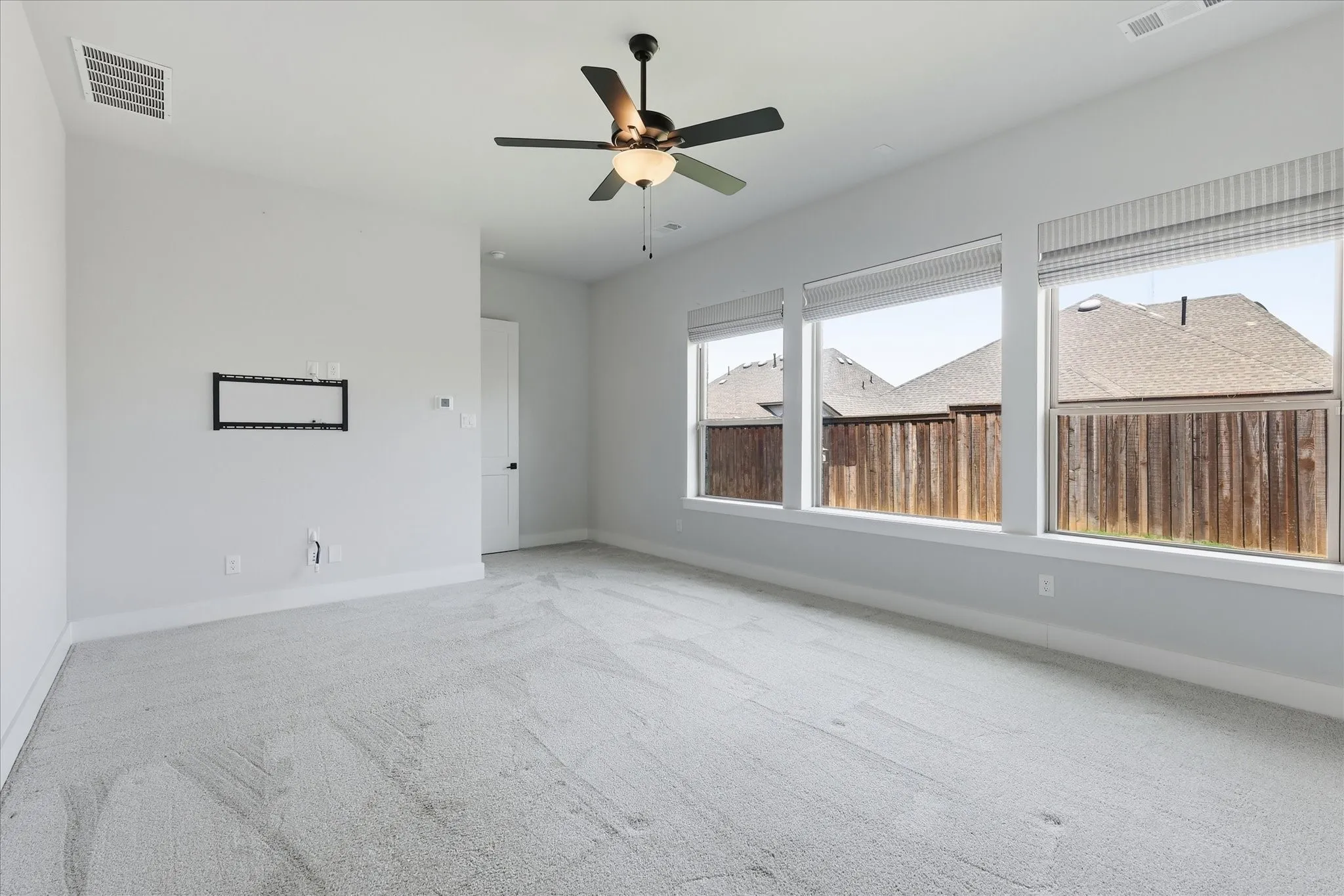 Spacious room featuring light-toned carpeting, multiple large windows, a ceiling fan with integrated lighting, and a neutral wall color