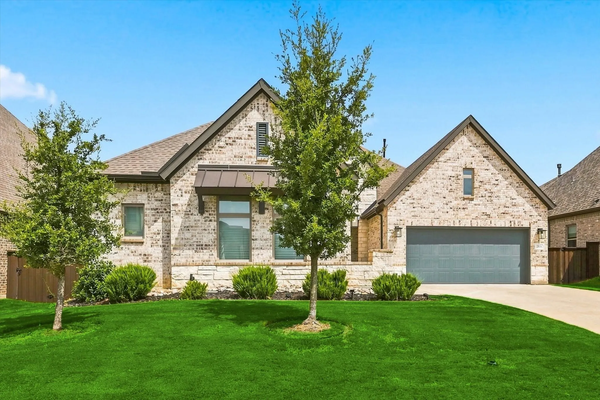 Brick and stone exterior with a gray garage door, featuring a pitched roof and a manicured lawn