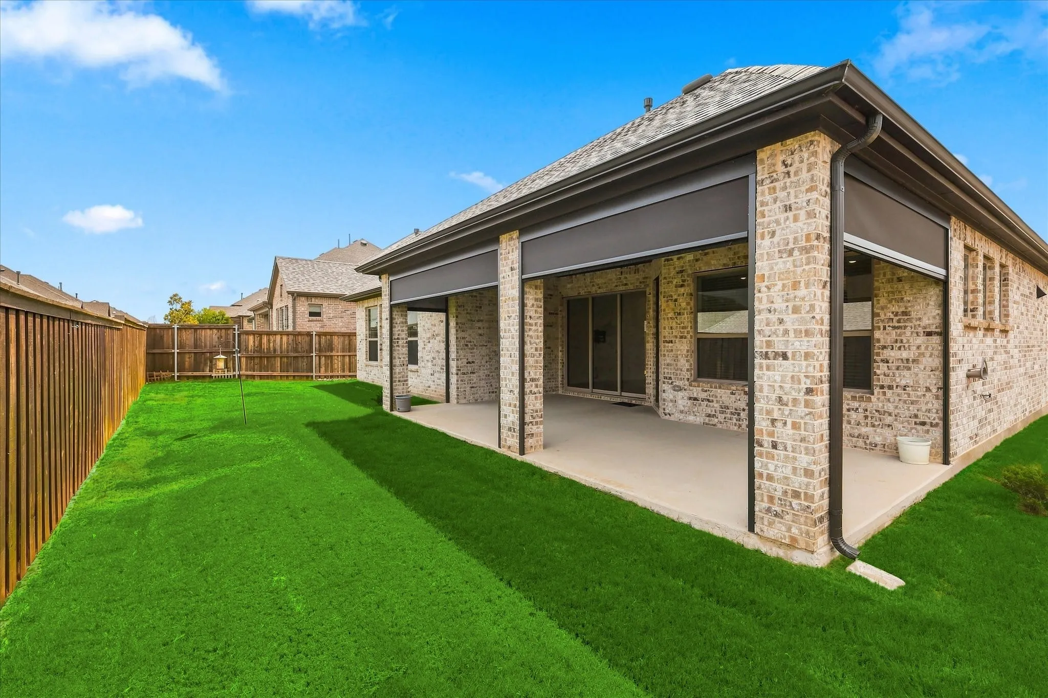 Expansive backyard featuring a manicured lawn, wood fencing, and a covered patio with privacy screens