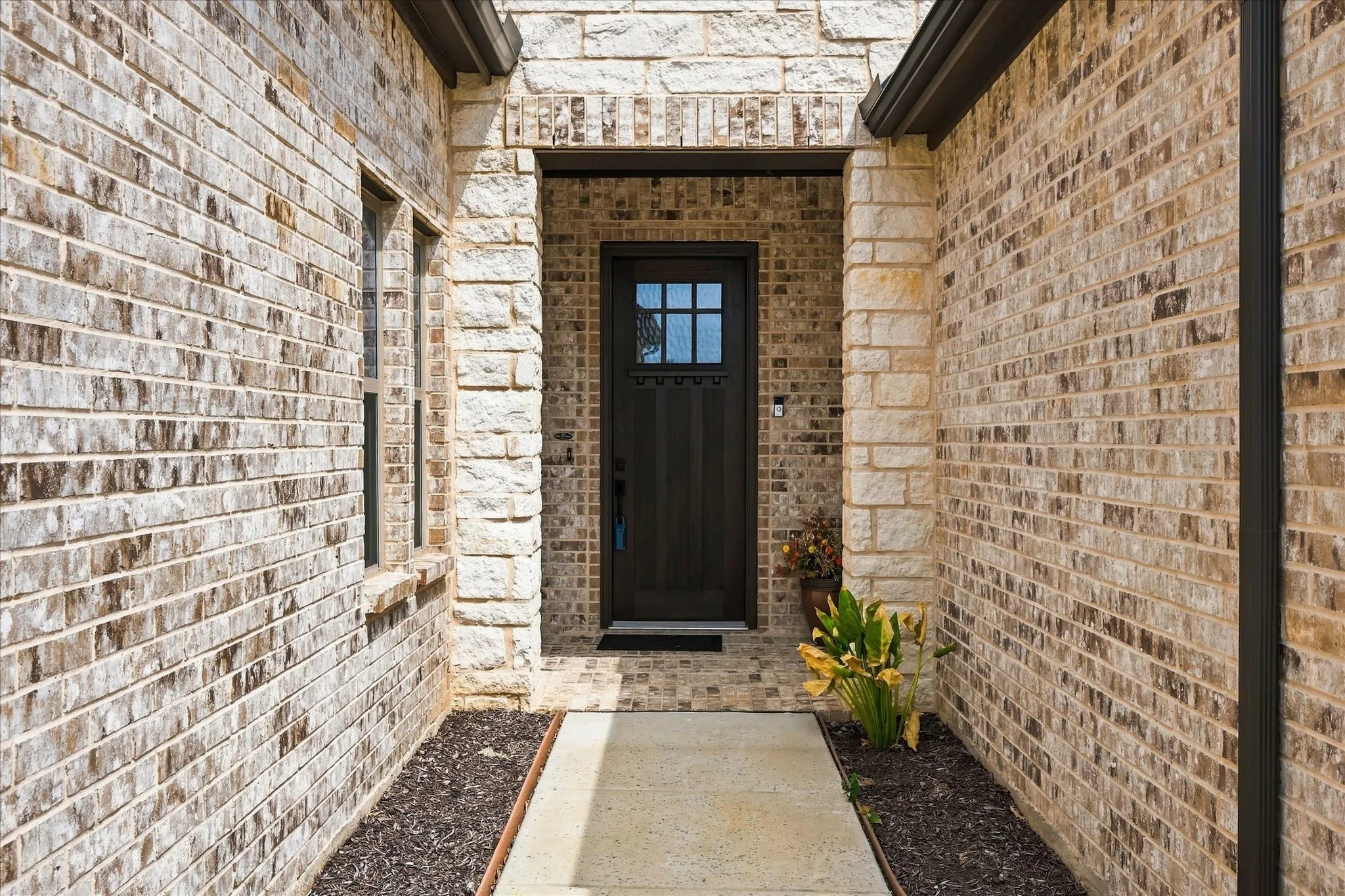 Stone and brick veneer exterior featuring a dark wood-finish entry door with glass inserts and a covered porch