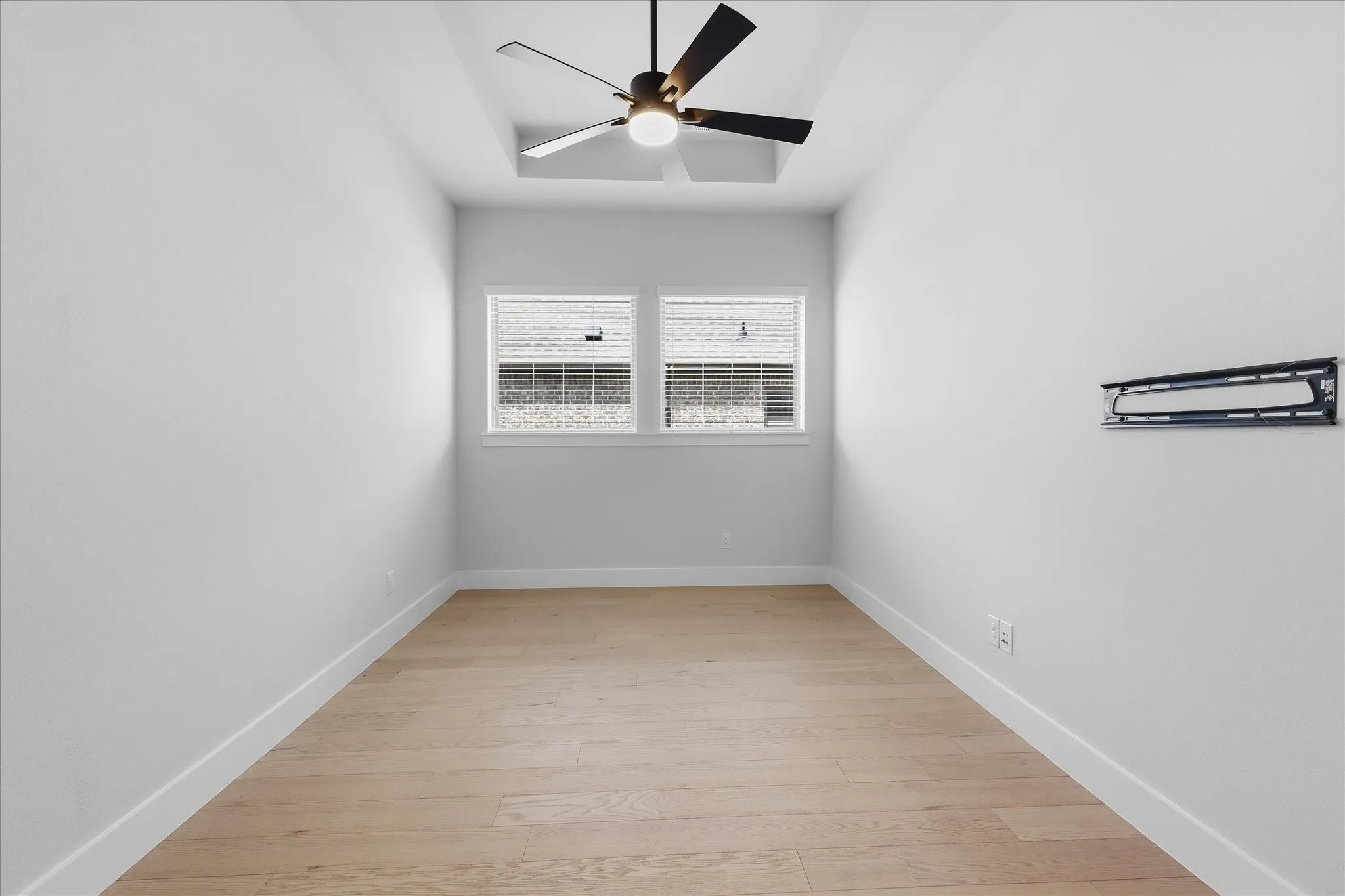 Recessed ceiling detail with a ceiling fan, dual windows, and wood-finish flooring