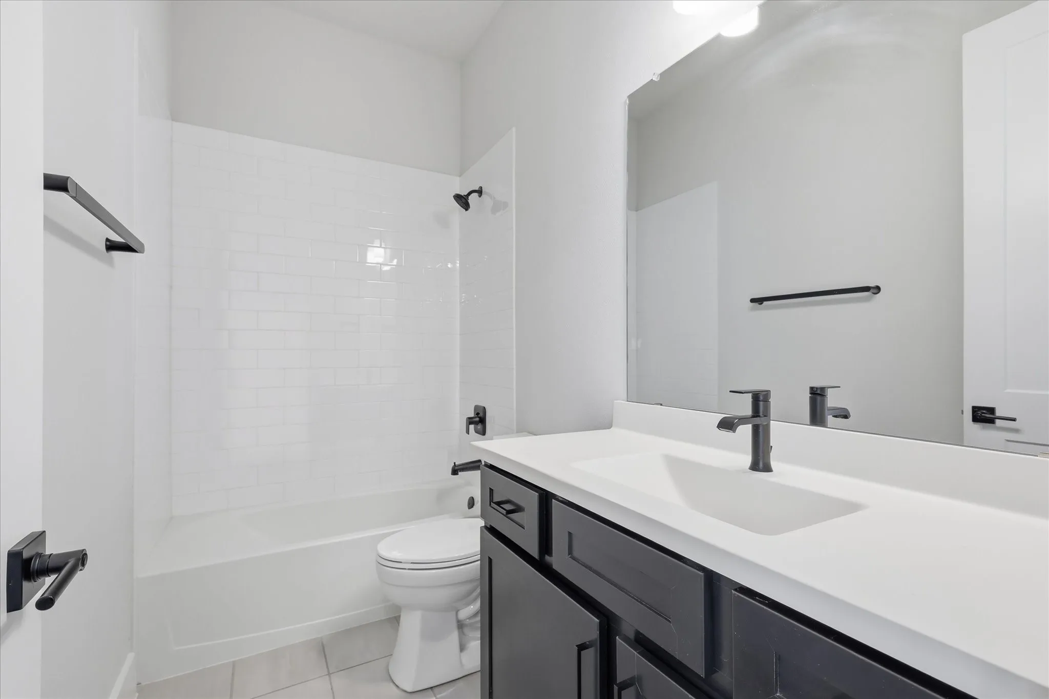 Bathroom featuring a white subway tile shower surround, dark vanity with an integrated sink and white countertop, and matte black fixtures