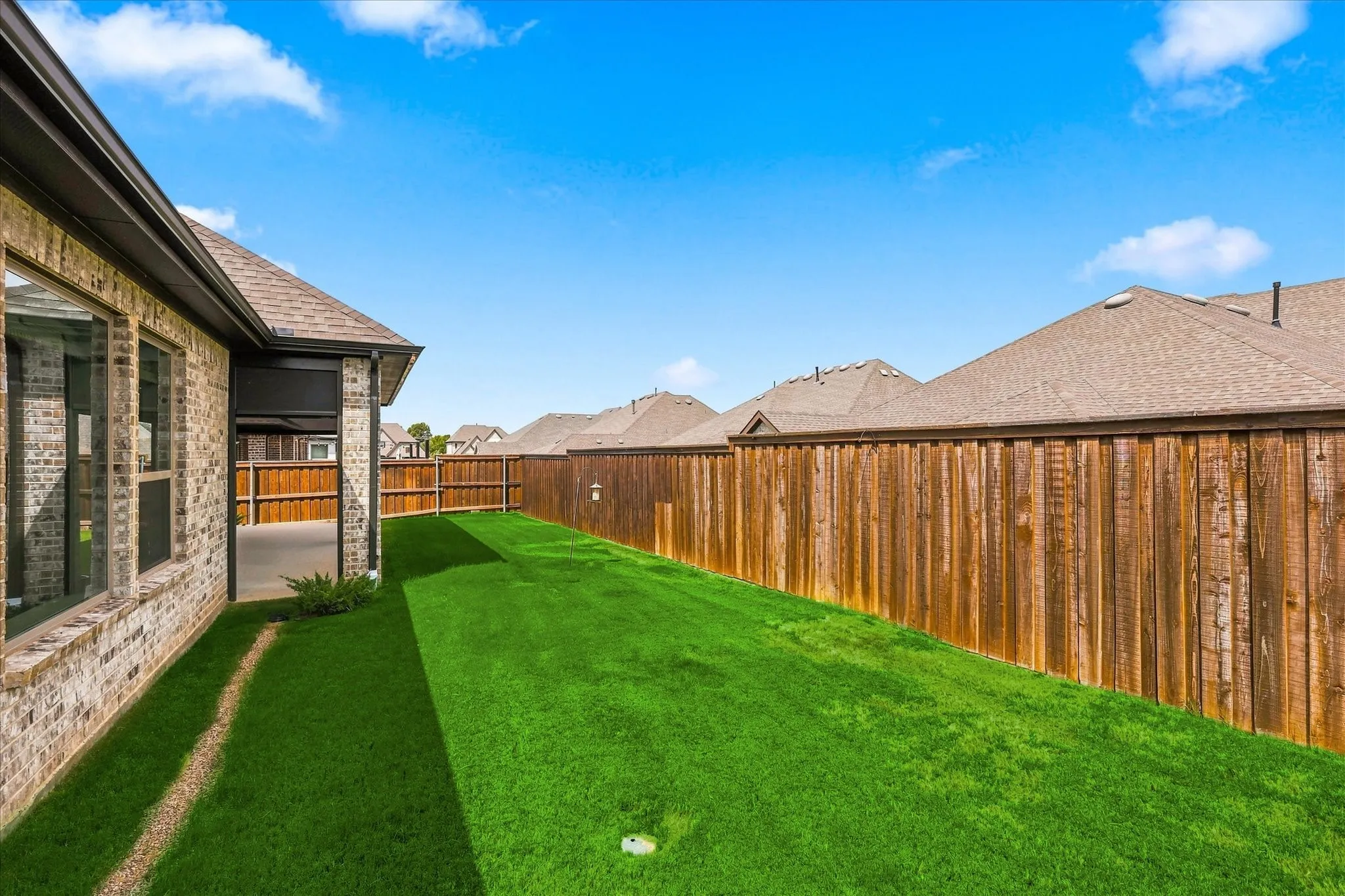Brick exterior with multiple windows, covered patio, wood fencing, and a manicured lawn