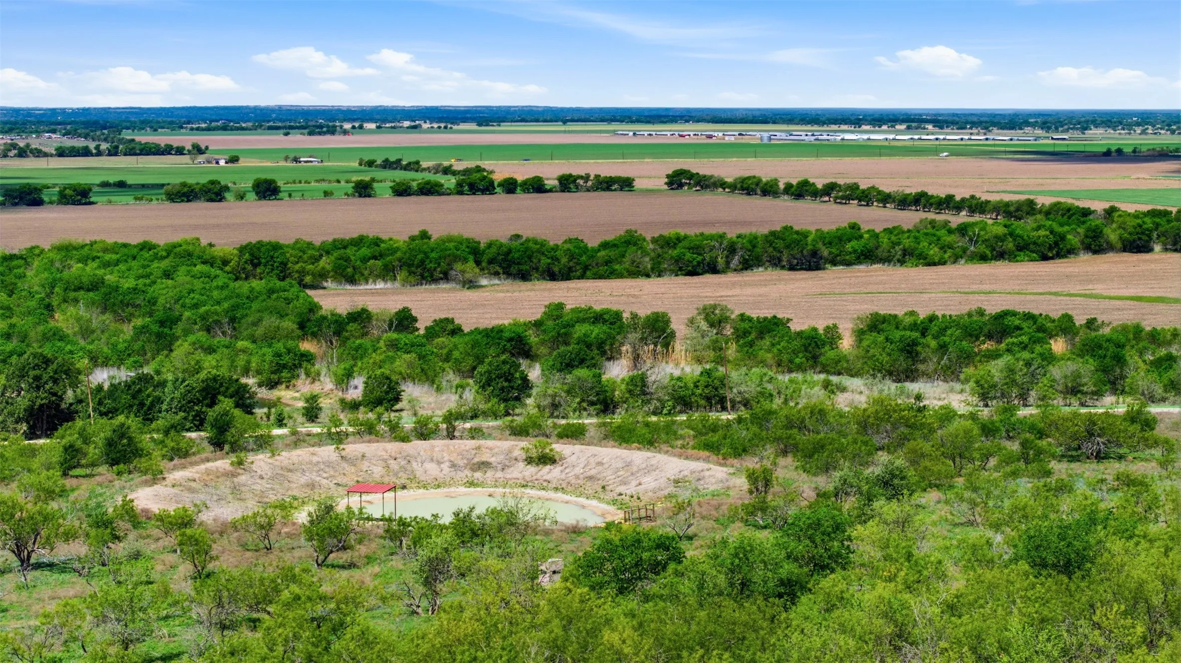 Expansive natural landscape featuring a pond, surrounding trees, and cultivated fields