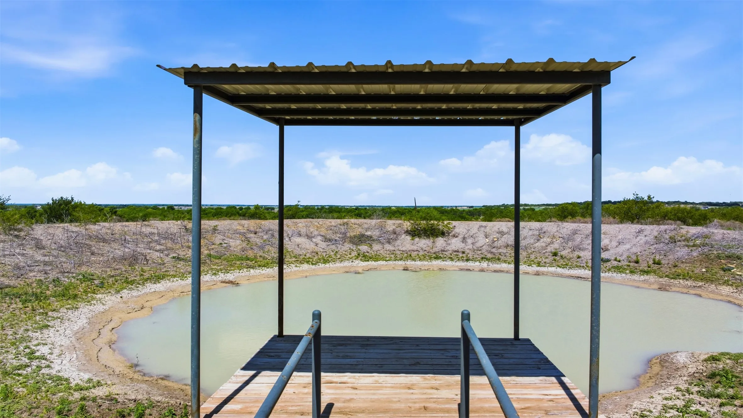 Shaded dock structure with metal roofing and handrails overlooking a water feature