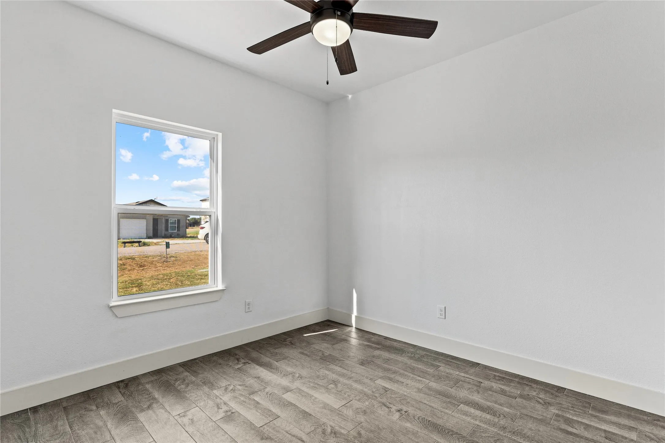 Modern ceiling fan with dark wood-finish blades, wood-finish flooring, white walls, and a single window