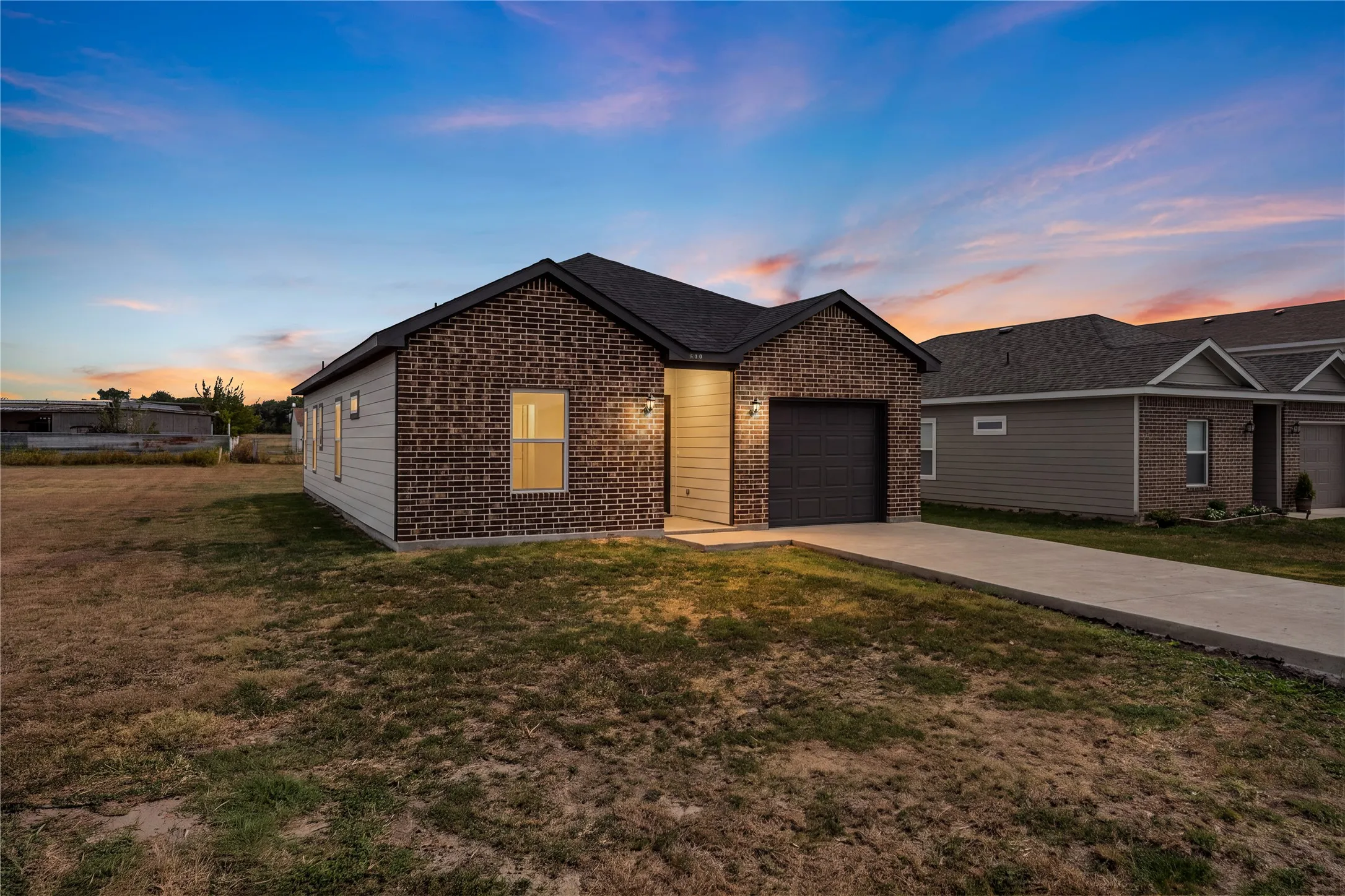 Brick and siding exterior with an attached garage, concrete driveway, and exterior lighting