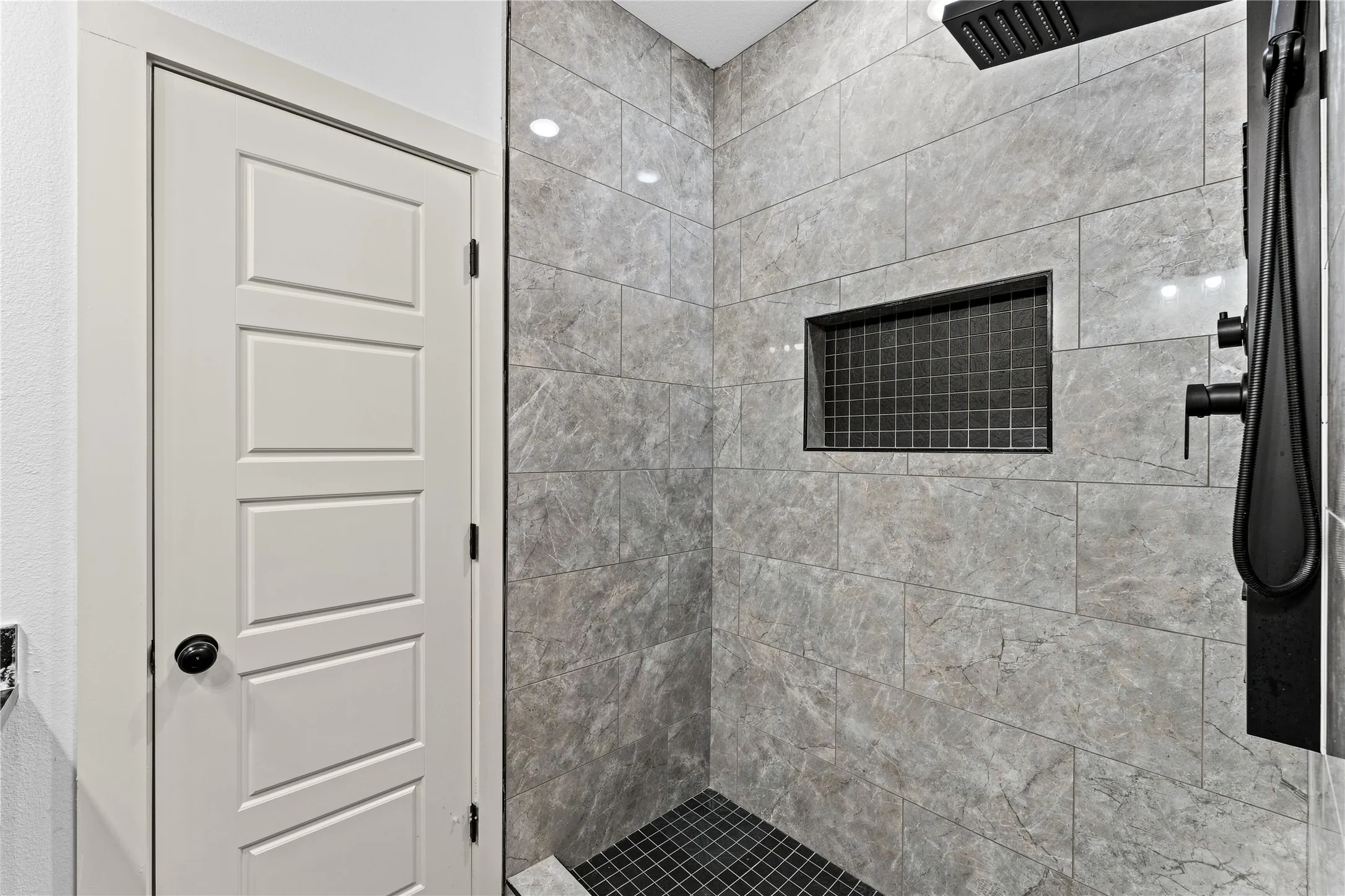 Tiled shower with a built-in niche, rain shower head, hand-held shower, and matte black fixtures