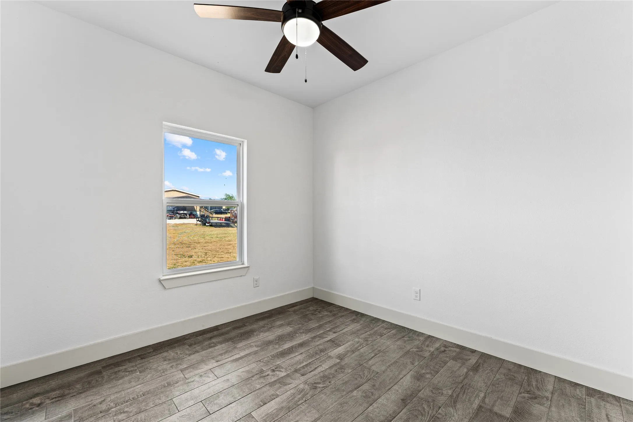 Wood-finish flooring, white walls, single window, and a ceiling fan with integrated lighting