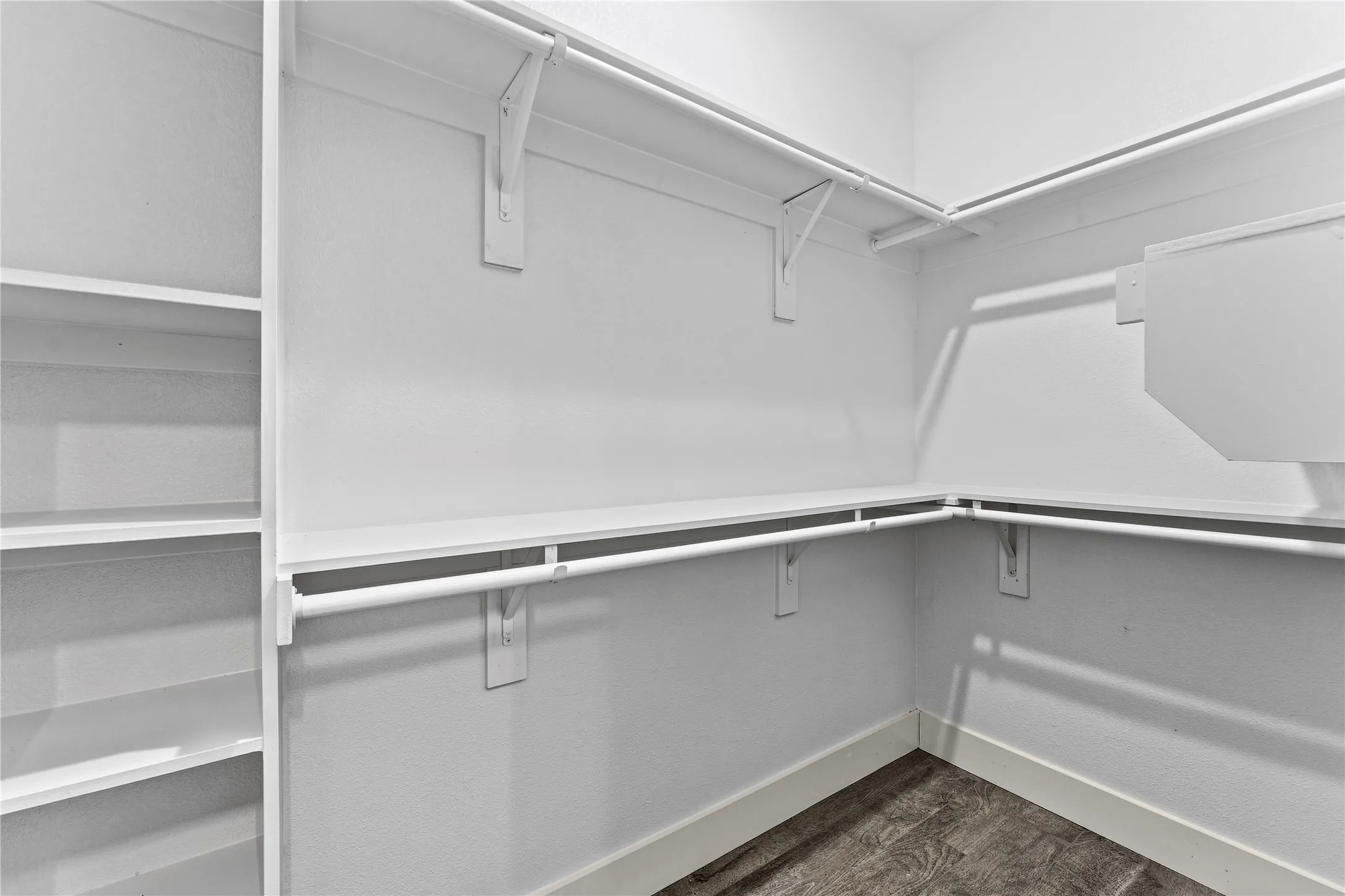Spacious walk-in closet featuring white painted walls, chrome hanging rods, and built-in shelving with multiple storage compartments