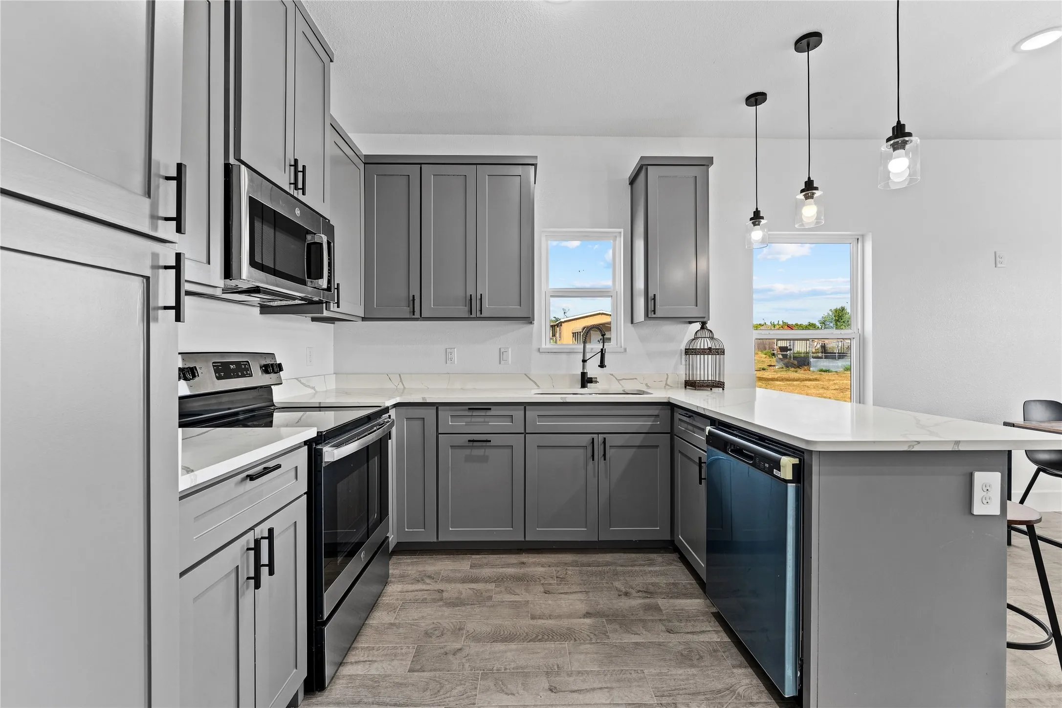 Modern kitchen featuring gray cabinetry, stainless steel appliances, light-toned countertops, and wood-finish flooring