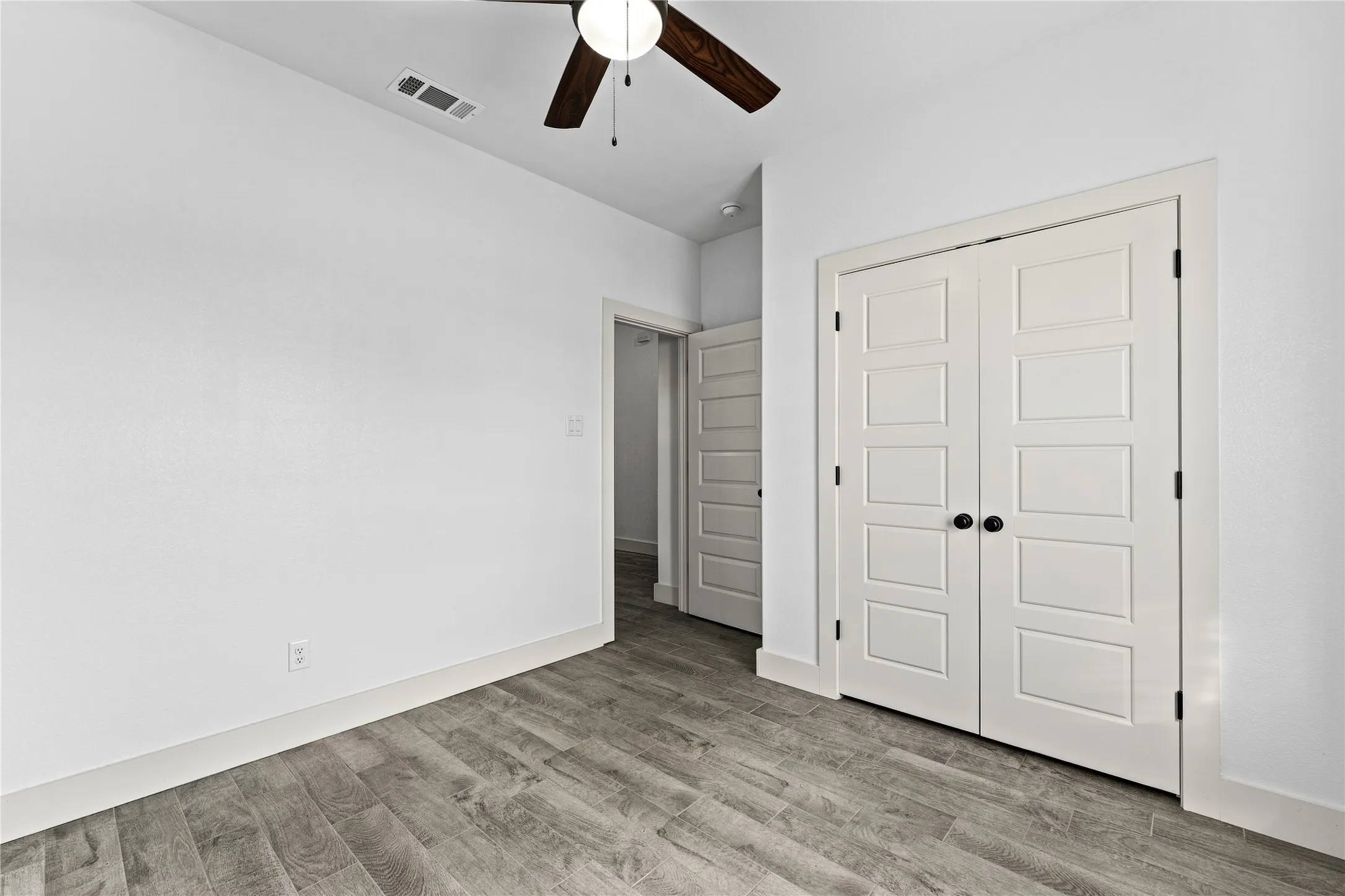 Wood-finish flooring, white paneled double doors with matte black hardware, and a ceiling fan