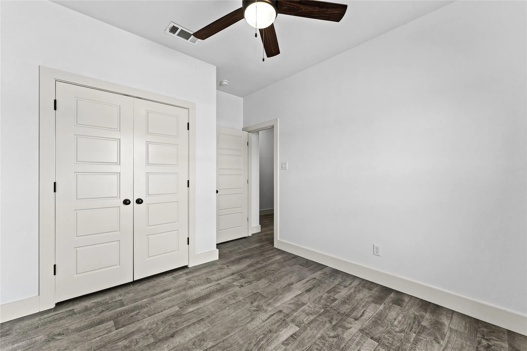 Wood-finish flooring with white baseboards, a ceiling fan, and white paneled doors