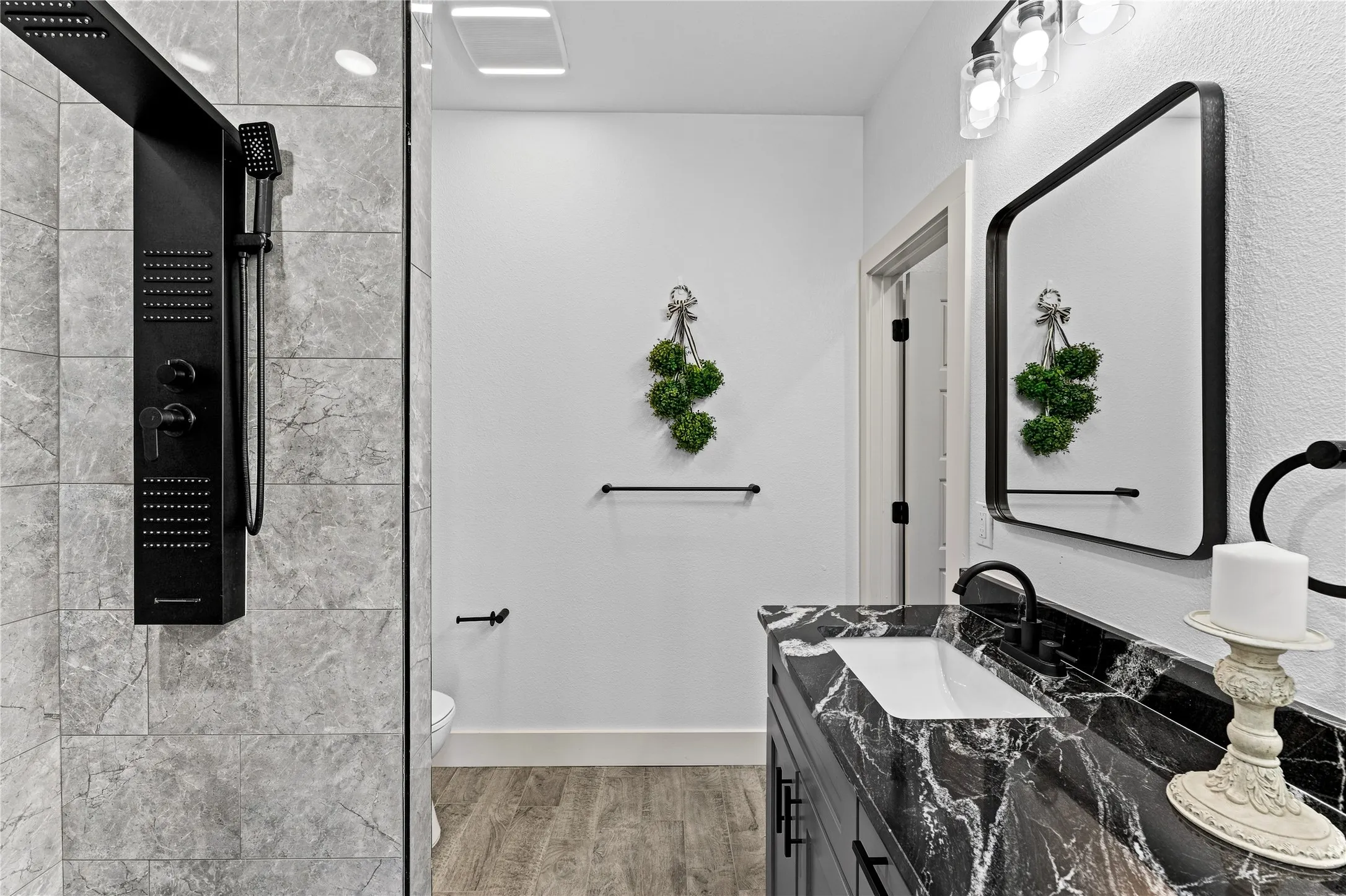Walk-in shower with a black shower panel, gray large format wall tiles, and a glass partition