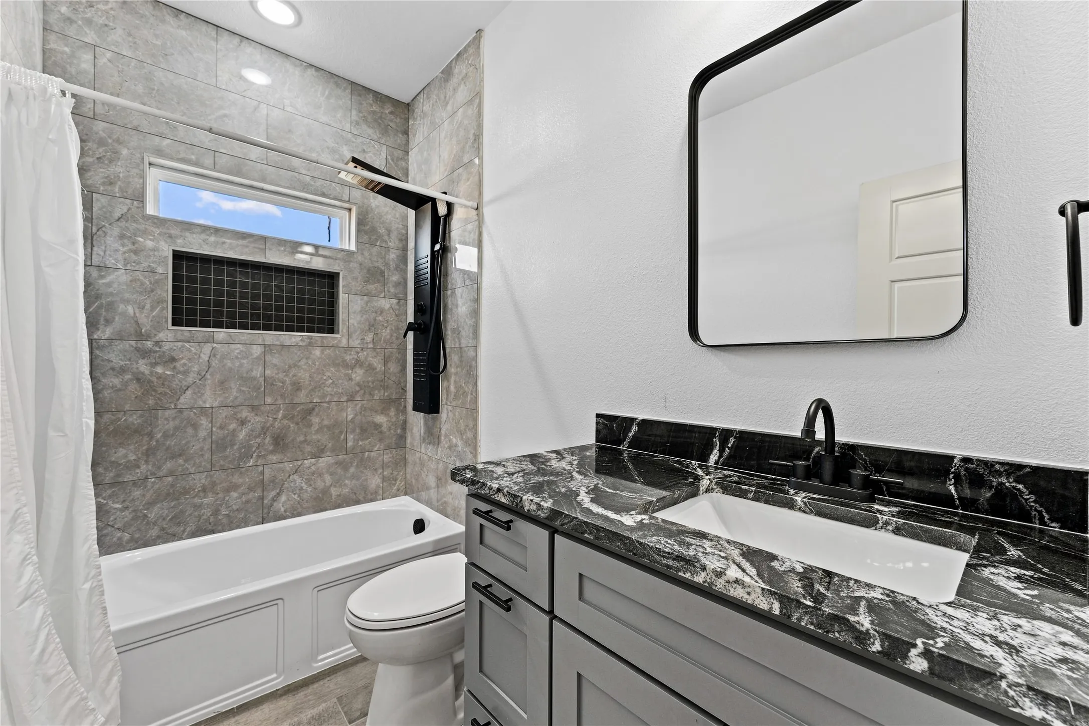 Rectangular bathtub with a tiled surround, integrated shower panel, and recessed niche