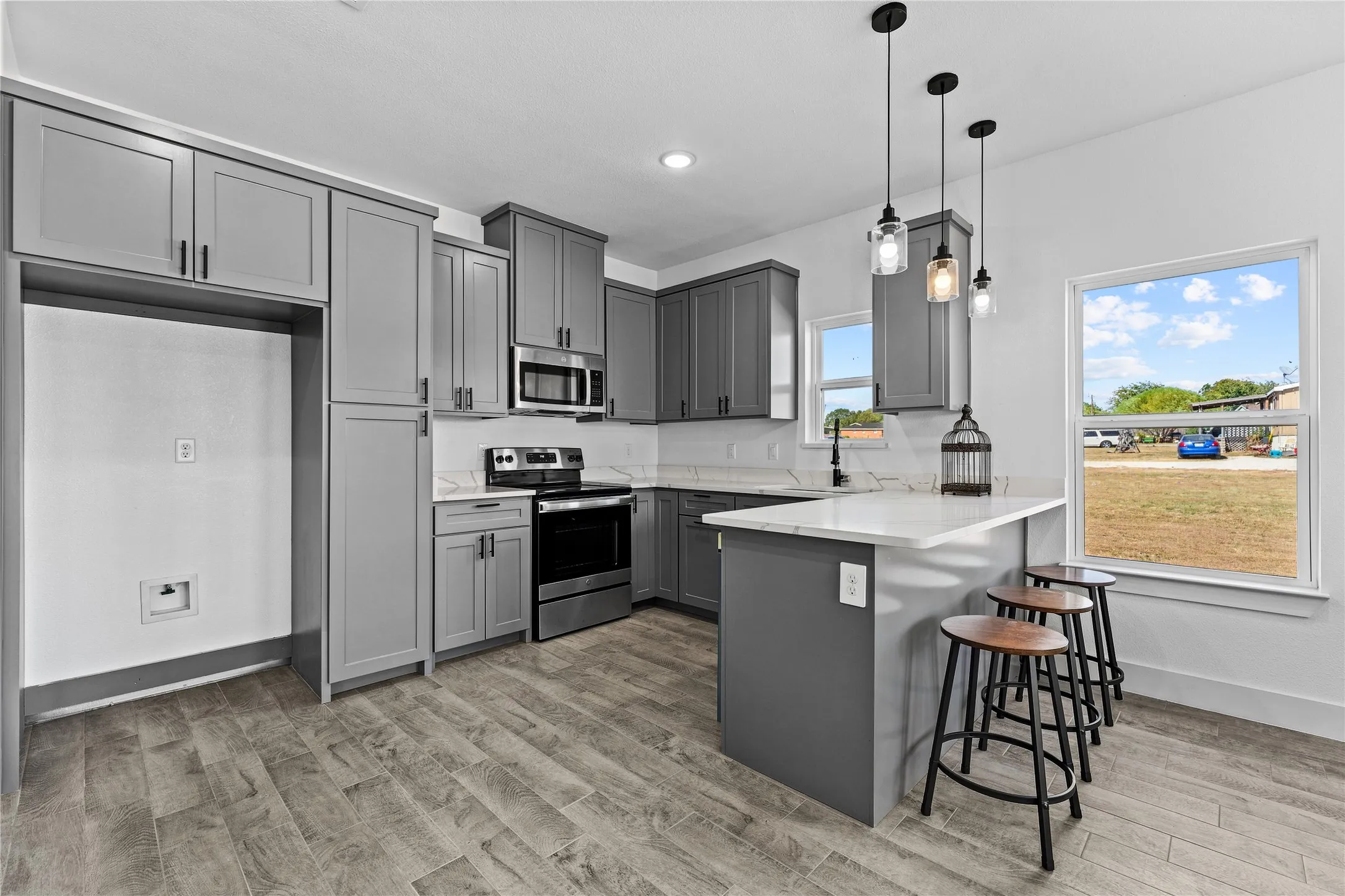 Kitchen featuring wood-finish flooring, gray cabinetry, stainless steel appliances, white countertops, and pendant lighting