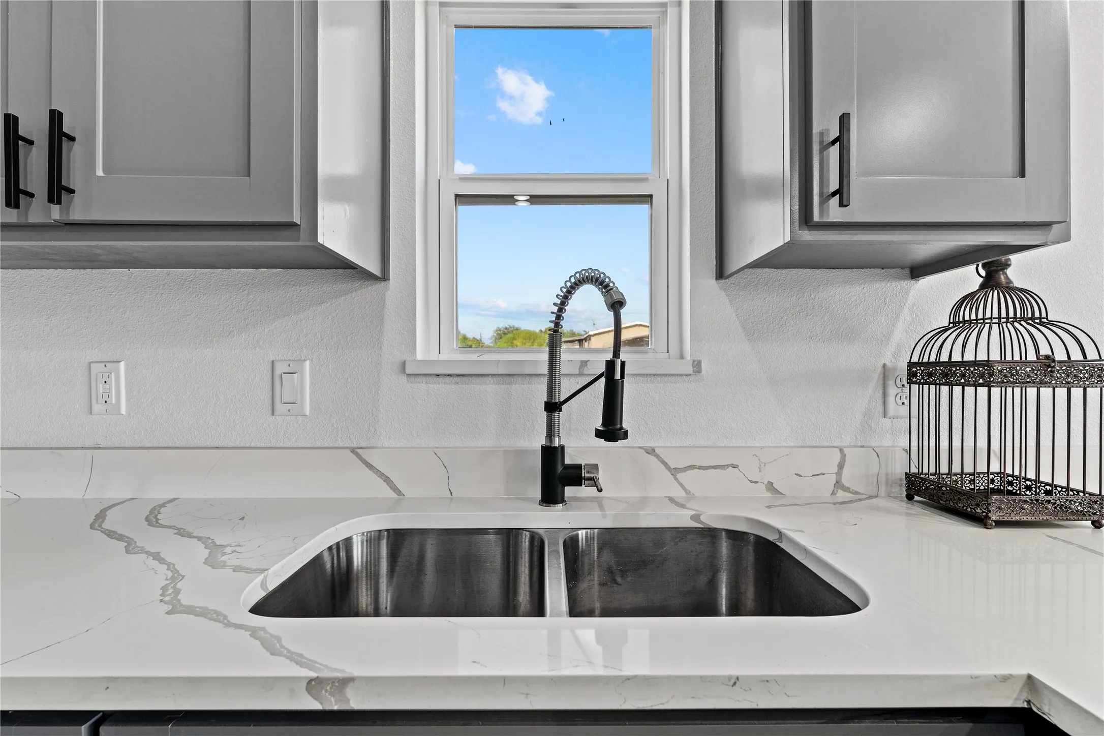 Stainless steel double-basin sink with a matte black high-arc faucet, quartz countertops, and gray upper cabinetry