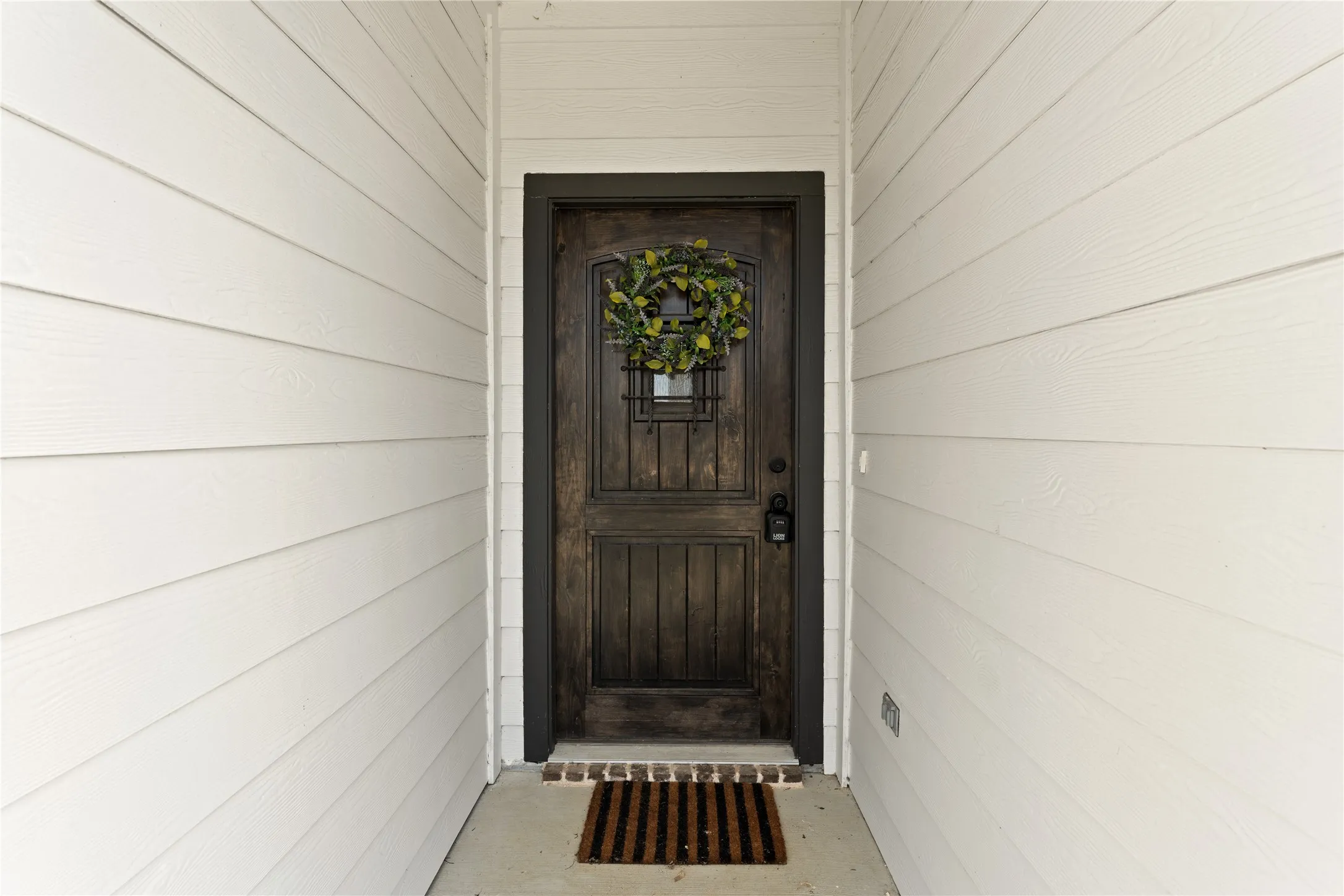 White horizontal siding, dark wood-finish entry door, and dark door trim
