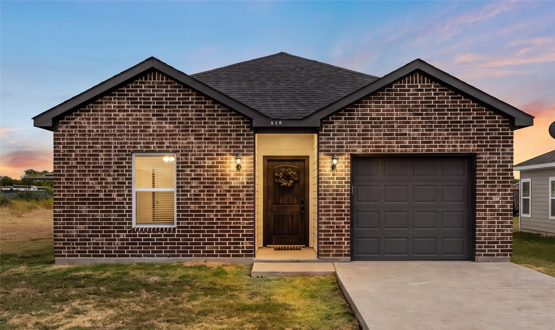 Brick exterior with dark gray garage door, concrete driveway, and covered entry