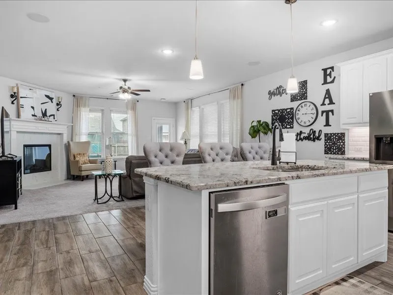 Open-concept layout featuring a kitchen island with seating, stainless steel dishwasher, white cabinetry, and granite countertops