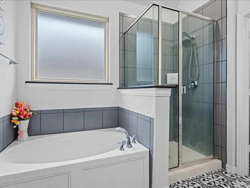 Soaking tub with deck-mounted chrome faucet, frosted window, and a separate glass-enclosed shower featuring dark-toned wall tiles