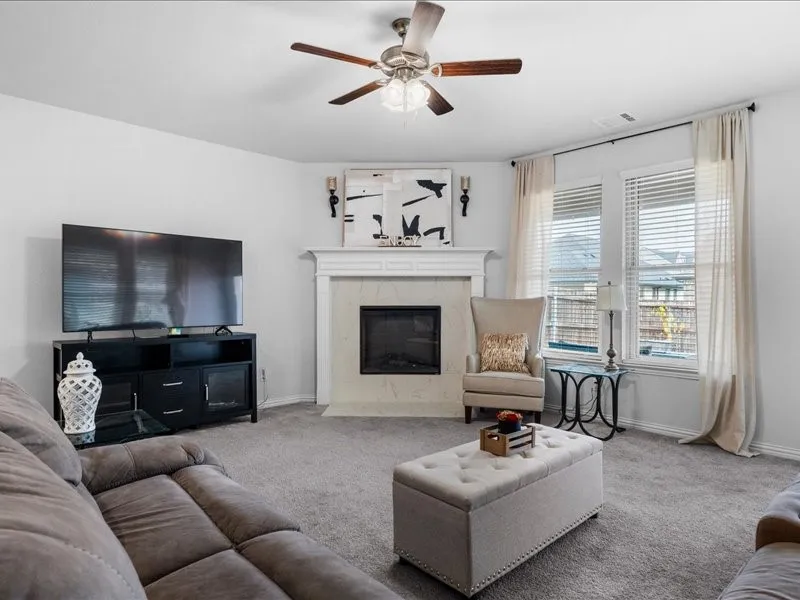 Carpeted living area featuring a ceiling fan, a fireplace with a mantel, and multiple windows