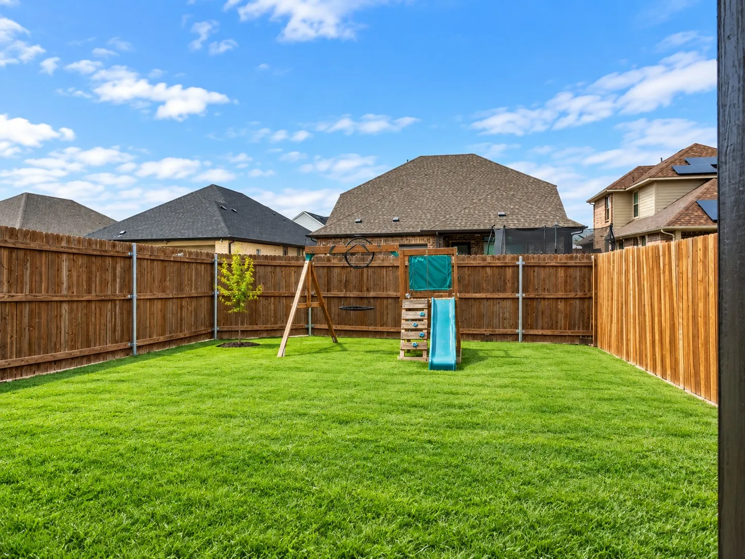 Expansive backyard featuring a manicured lawn, full privacy fencing, and a young deciduous tree